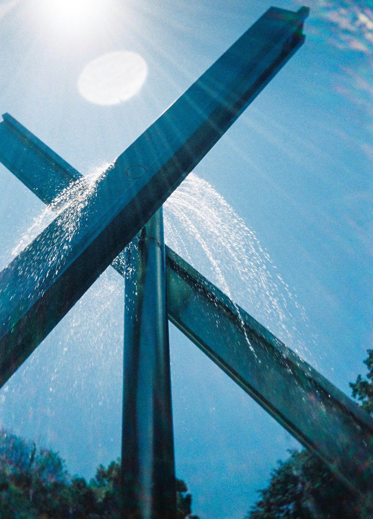 Metallskulptur mit Wasser, das unter einem klaren blauen Himmel spritzt
