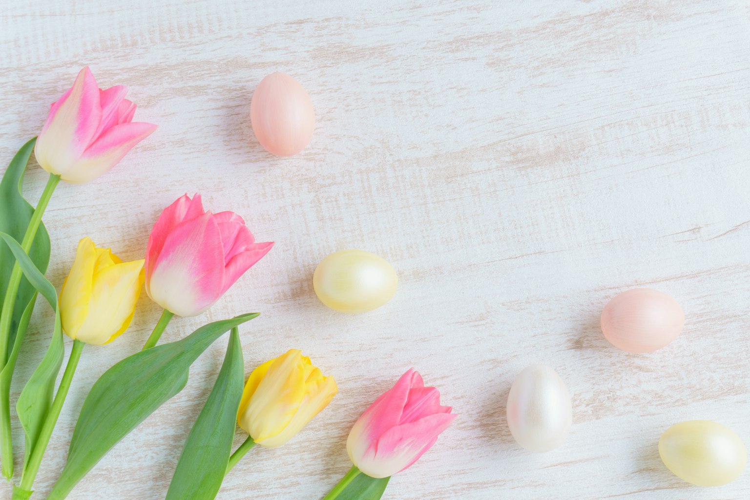 Arrangement of pink and yellow tulips with colorful eggs on a light wooden surface