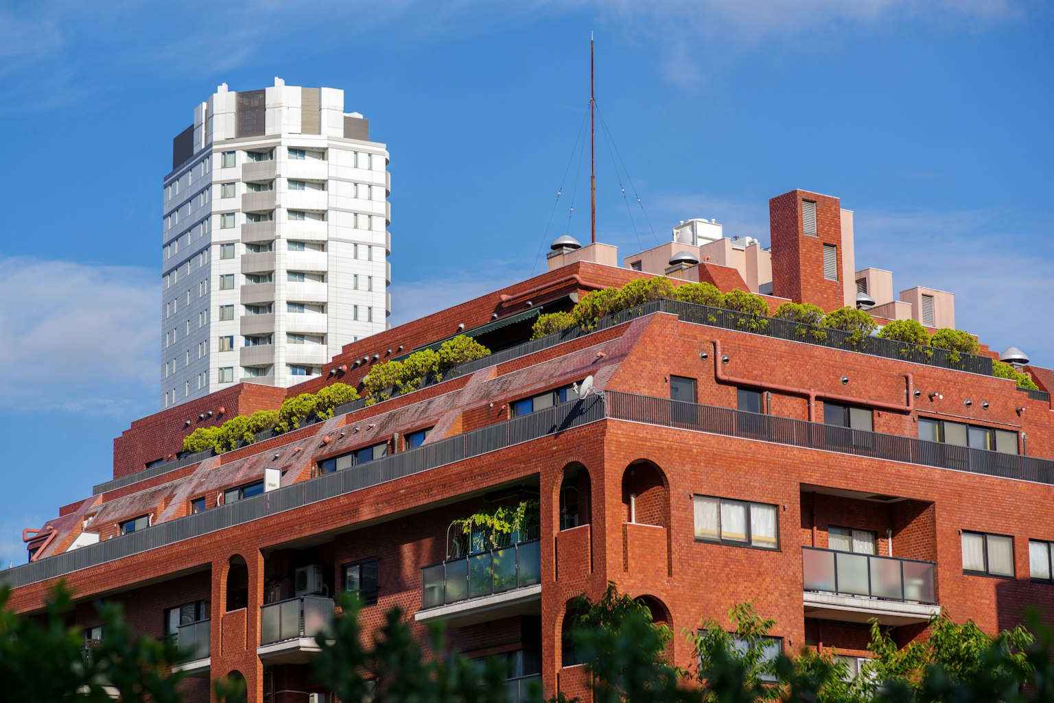 A red brick building with greenery on the roof alongside a modern high-rise under a blue sky