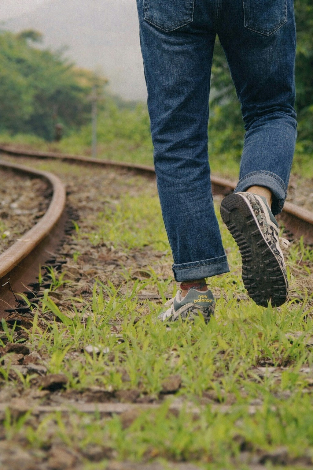 草に覆われた線路を歩く人の後ろ姿