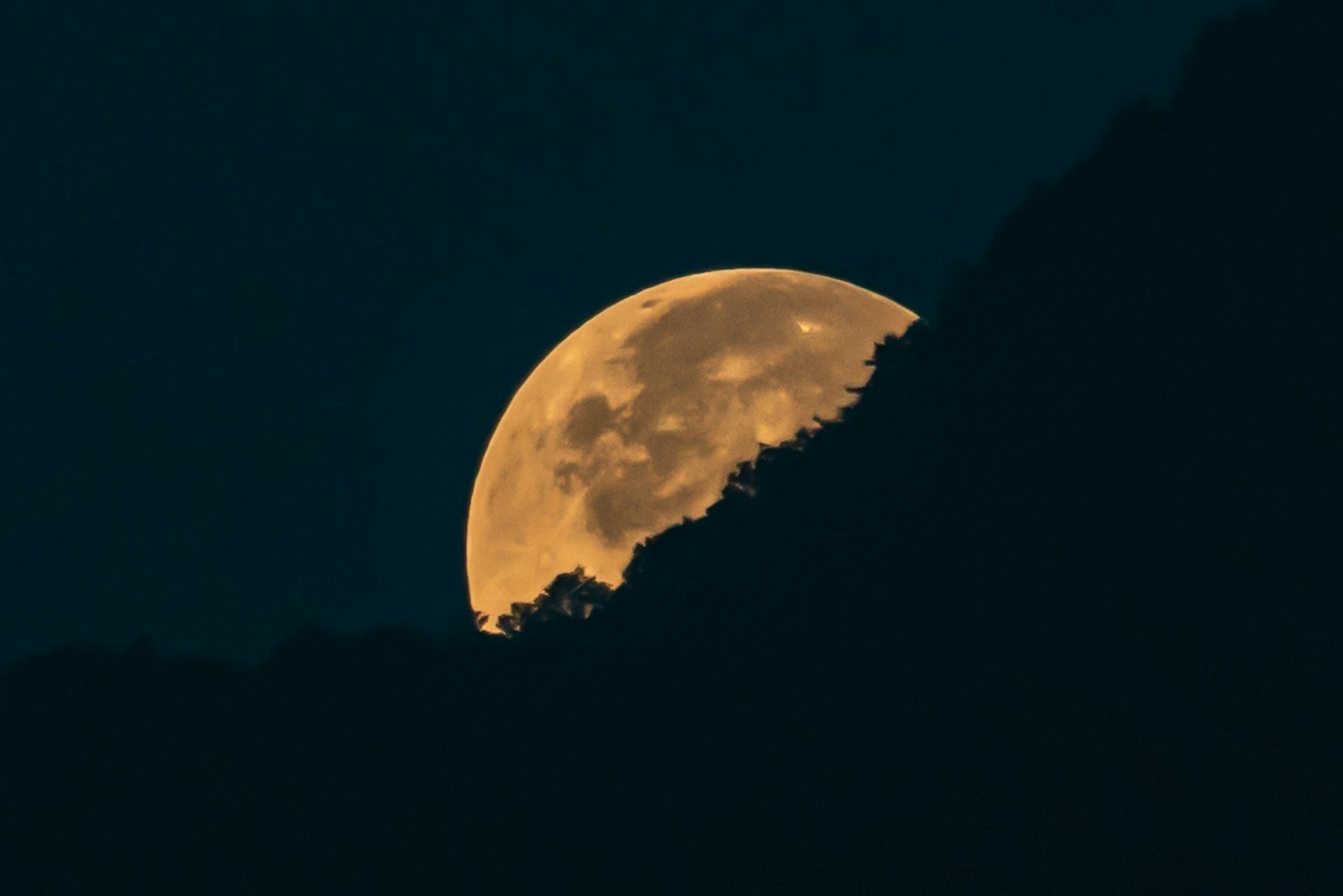 Luna arancione brillante che sorge su colline scure in silhouette