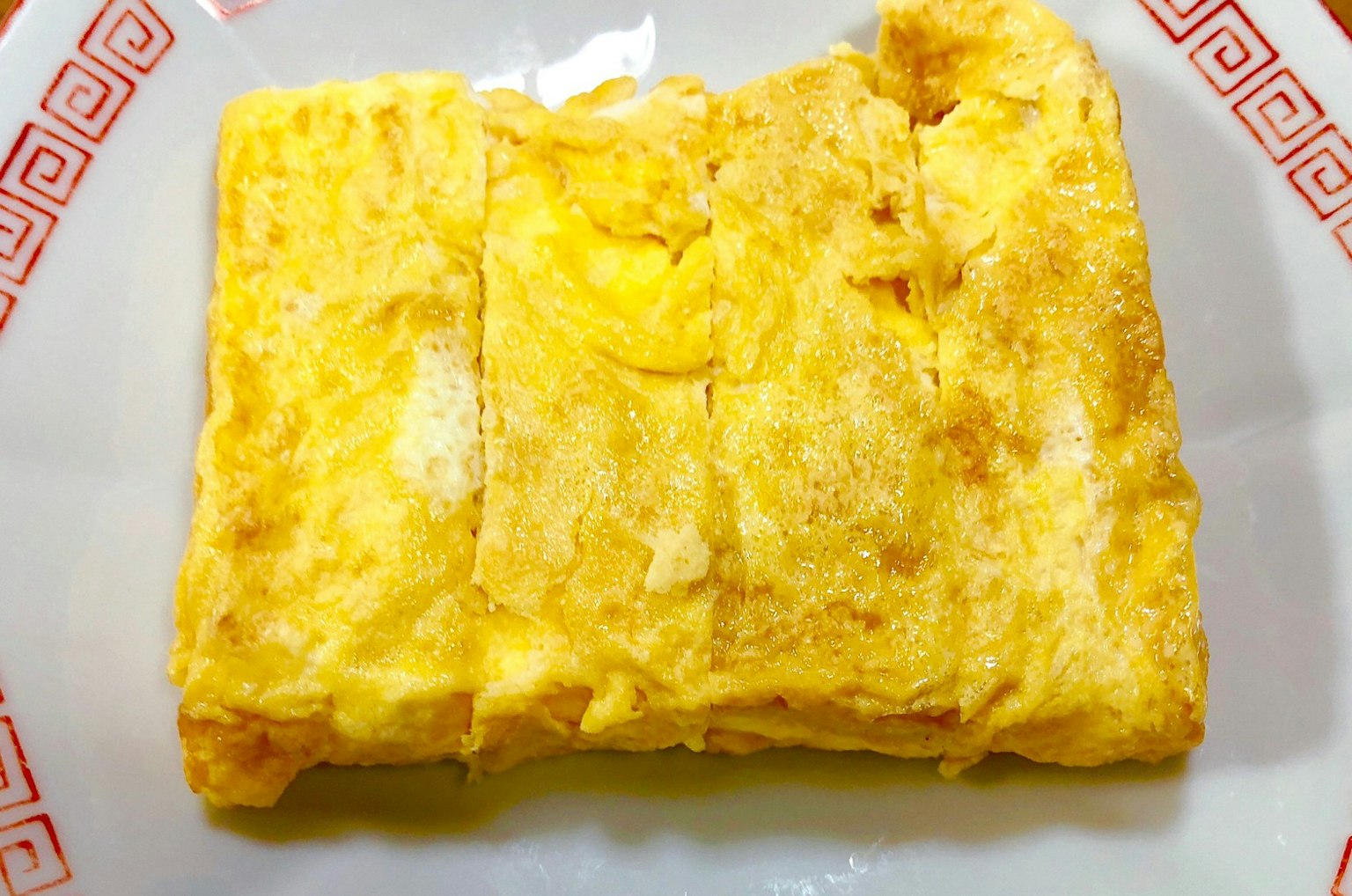 A rectangular block of Japanese omelette served on a white plate