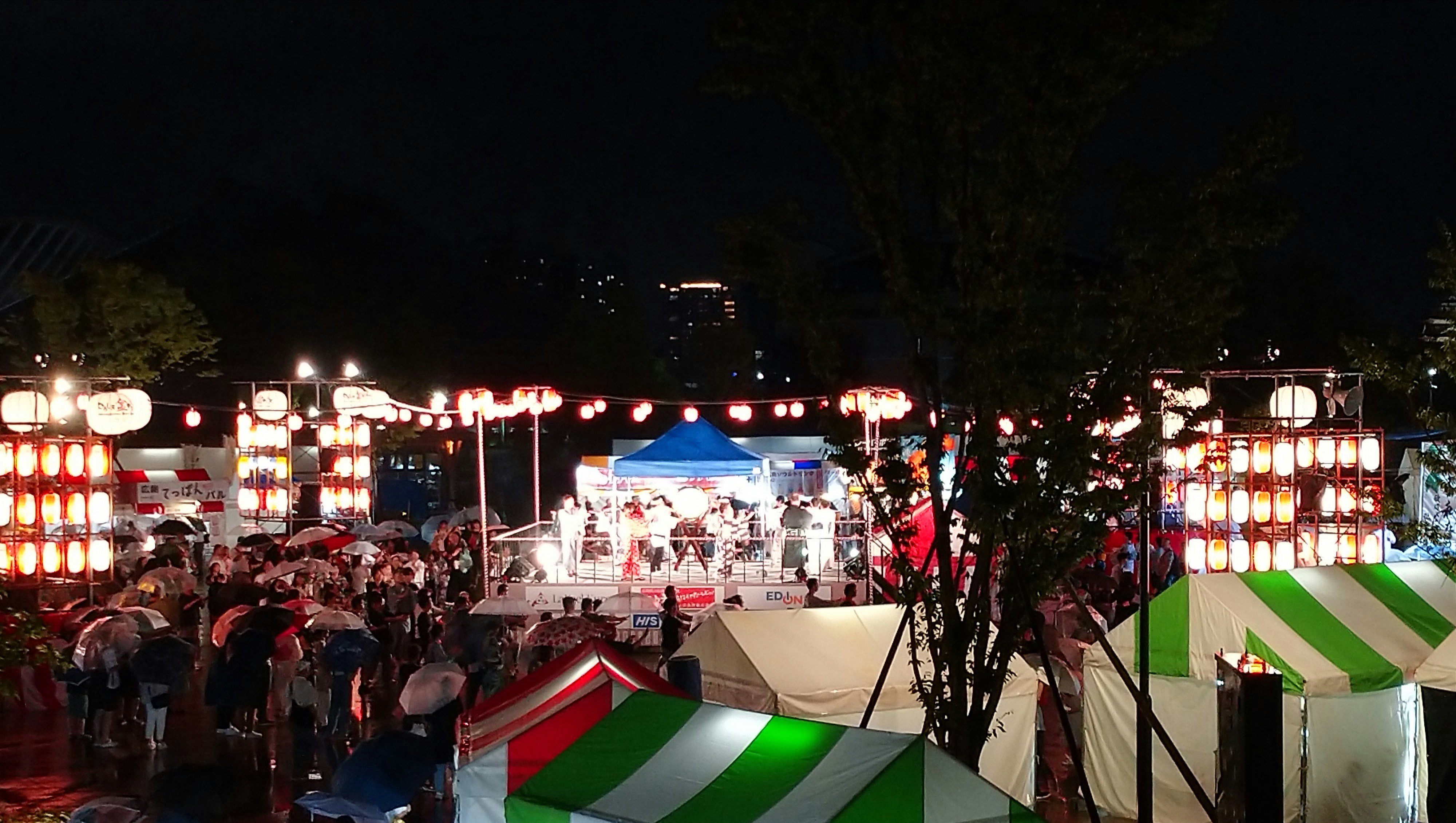 雨降りの盆踊り大会の屋台と提灯が並ぶ夜の会場