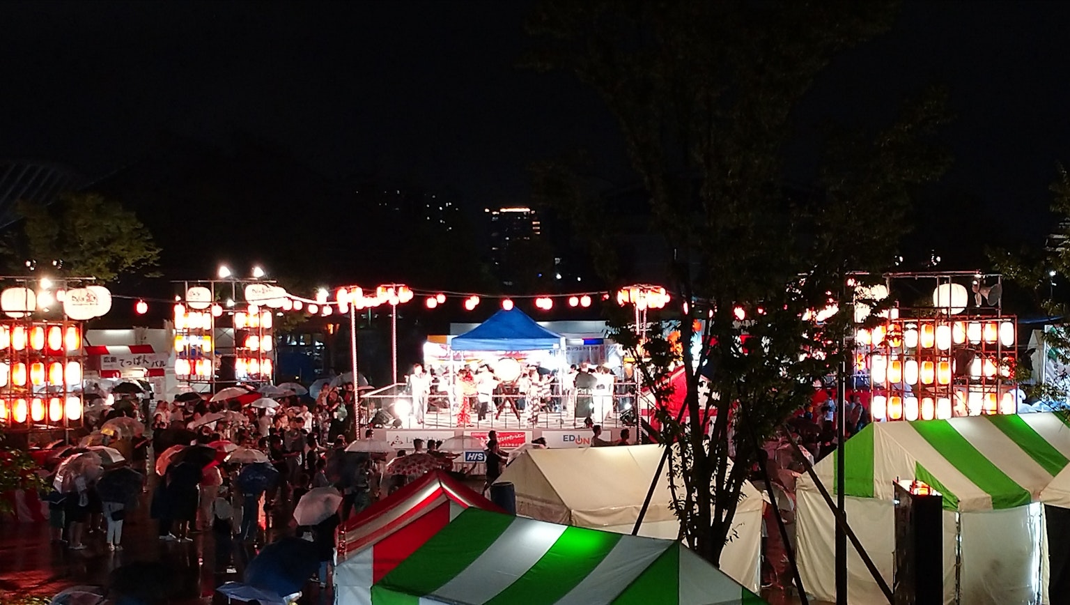 조명이 켜진 등불과 다채로운 천막으로 둘러싸인 공연 무대가 있는 야간 축제 장면