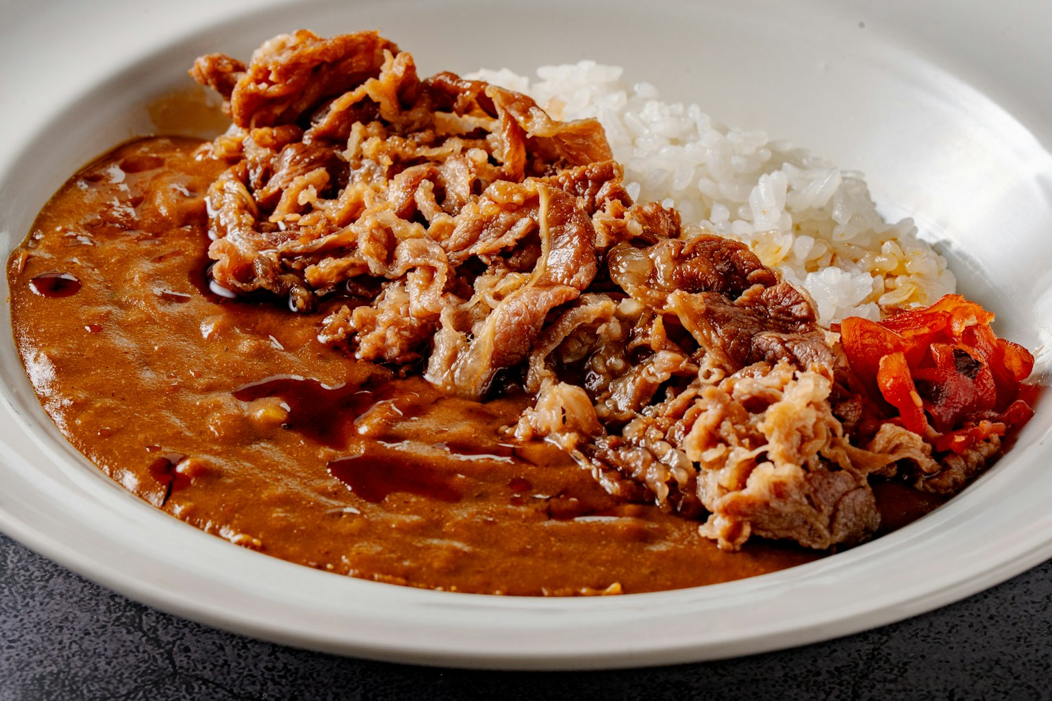 Un plato de arroz con un guiso de carne al curry y un acompañamiento de verduras encurtidas
