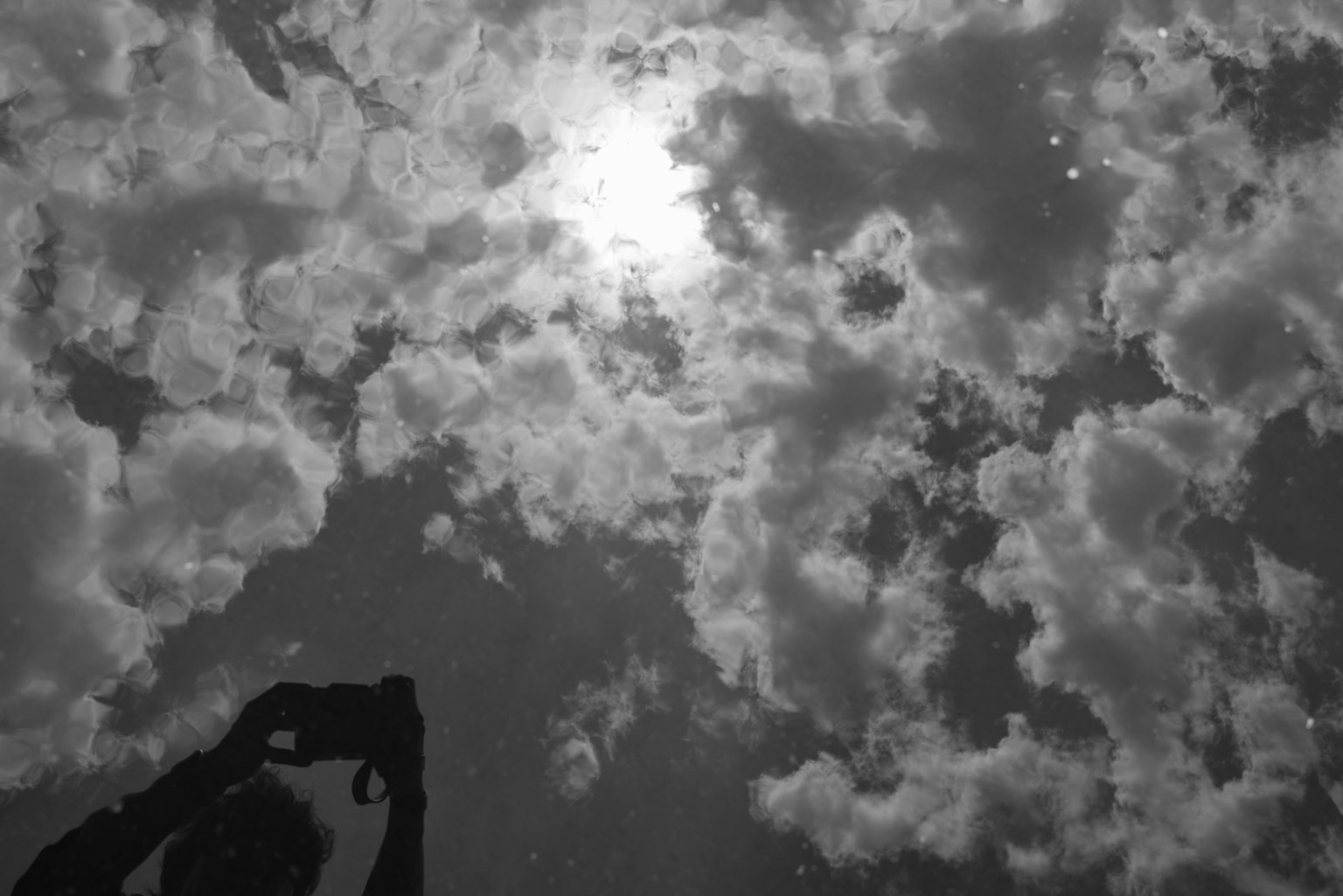 水面に映る雲と太陽の反射を捉えたモノクロの画像