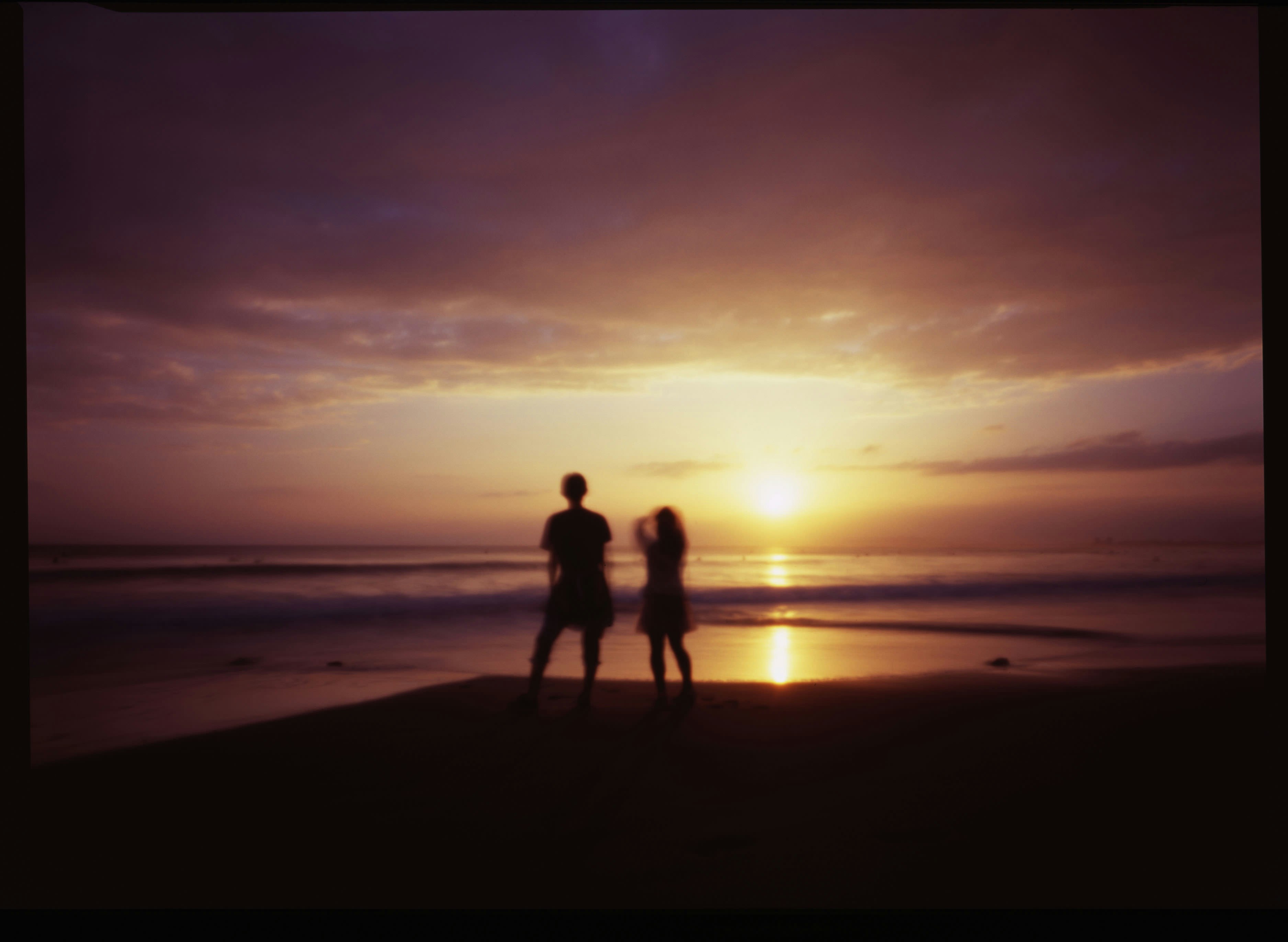 夕日に照らされた海辺を歩くシルエットの2人