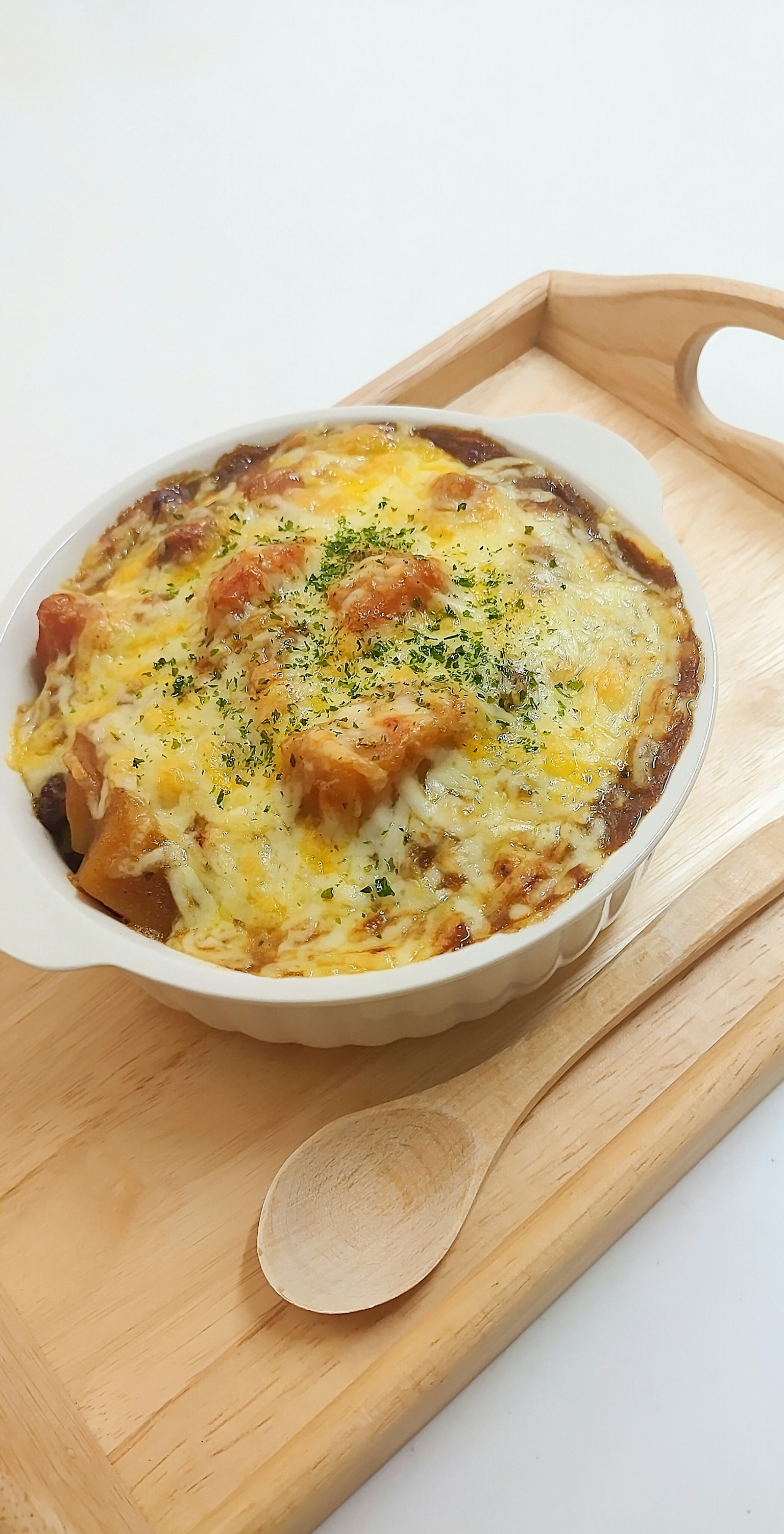 흰 접시에 담긴 구운 치즈 그라탱이 나무 쟁반에 놓여 있다