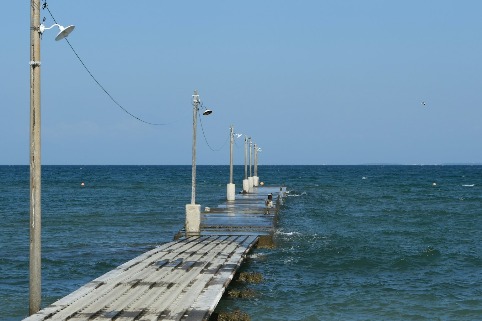 Holzsteg, der in das wellige Meer unter einem klaren blauen Himmel führt