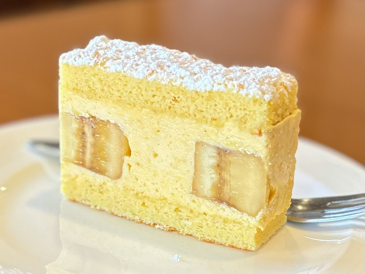 Irisan kue krim dengan isian pisang kue spons kuning ditaburi gula bubuk