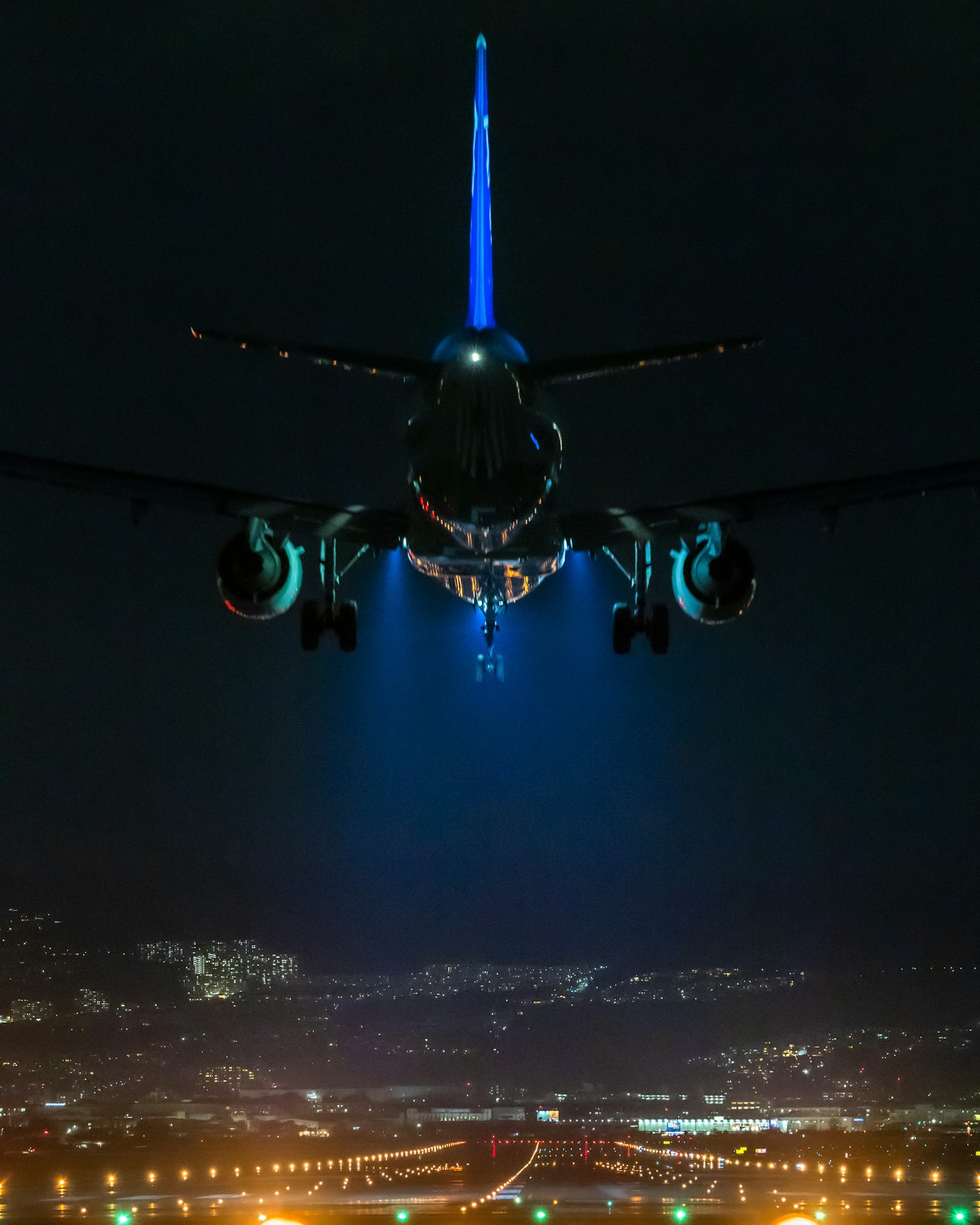 Vista posteriore di un aereo che vola di notte con luci della città sottostanti