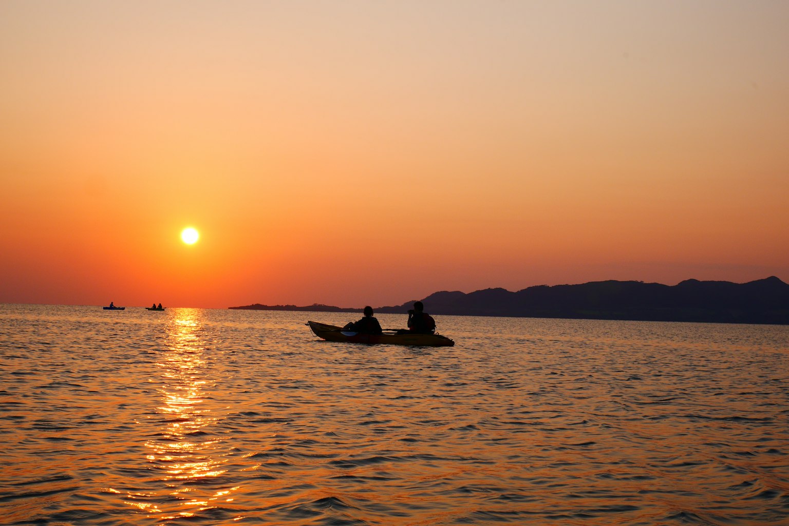Two fishermen in a small boat silhouetted against a sunset over the ocean