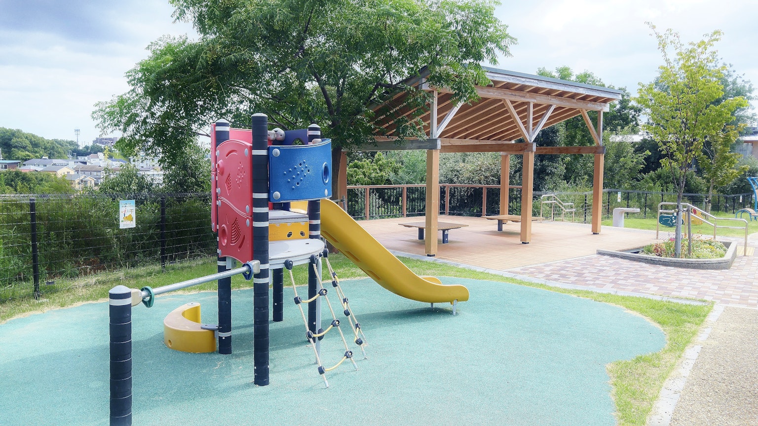 Un parque infantil colorido con un tobogán y un área cubierta con una estructura de madera