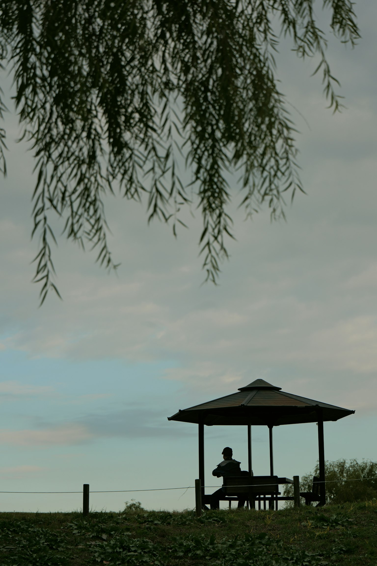Siluet seseorang yang duduk di paviliun di taman yang tenang