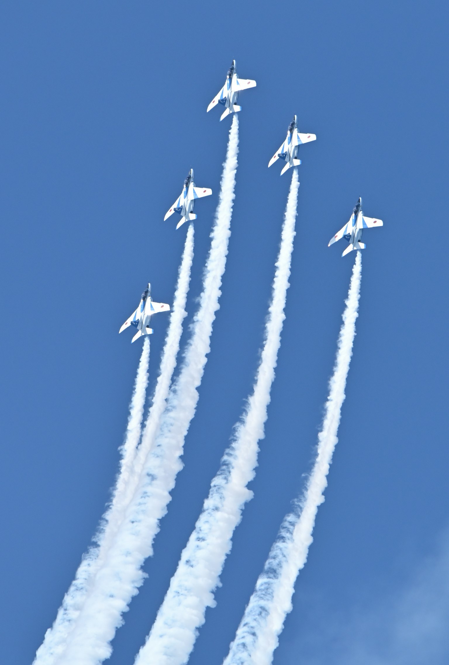 Cinco aviones de combate ascendiendo contra un cielo azul con estelas de humo blanco