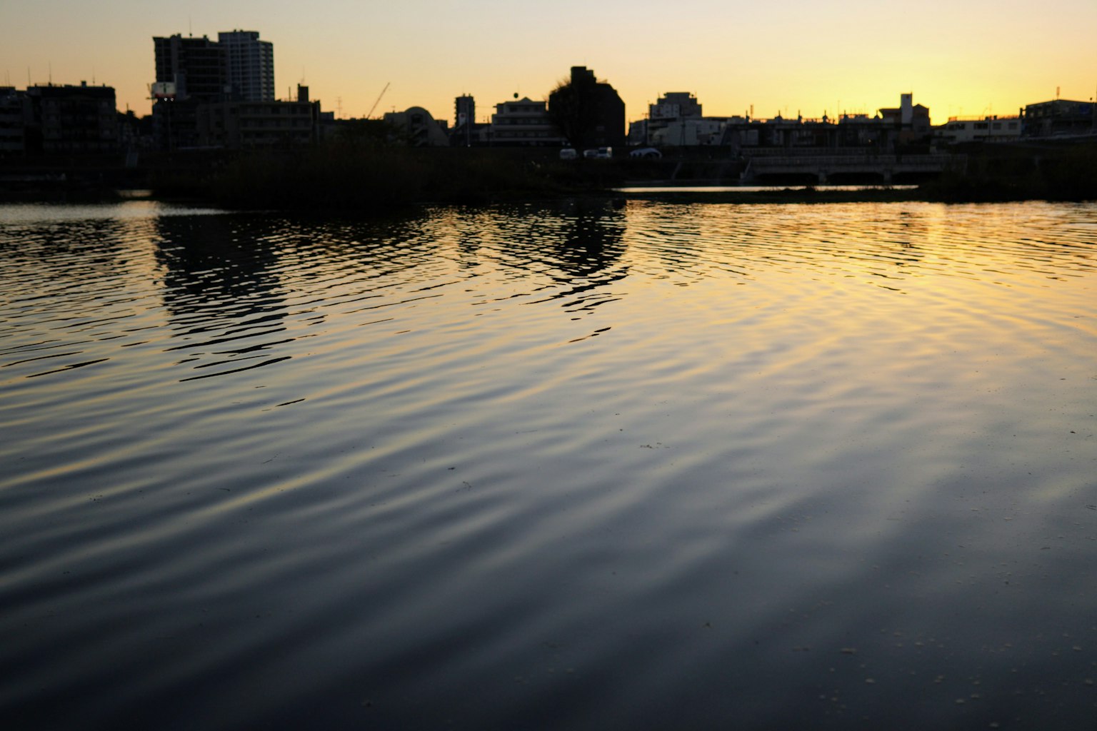 Lago sereno che riflette il tramonto con skyline cittadino in silhouette