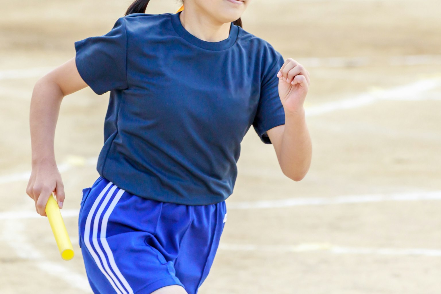 Niña corriendo con un testigo usando una camiseta y pantalones cortos azules