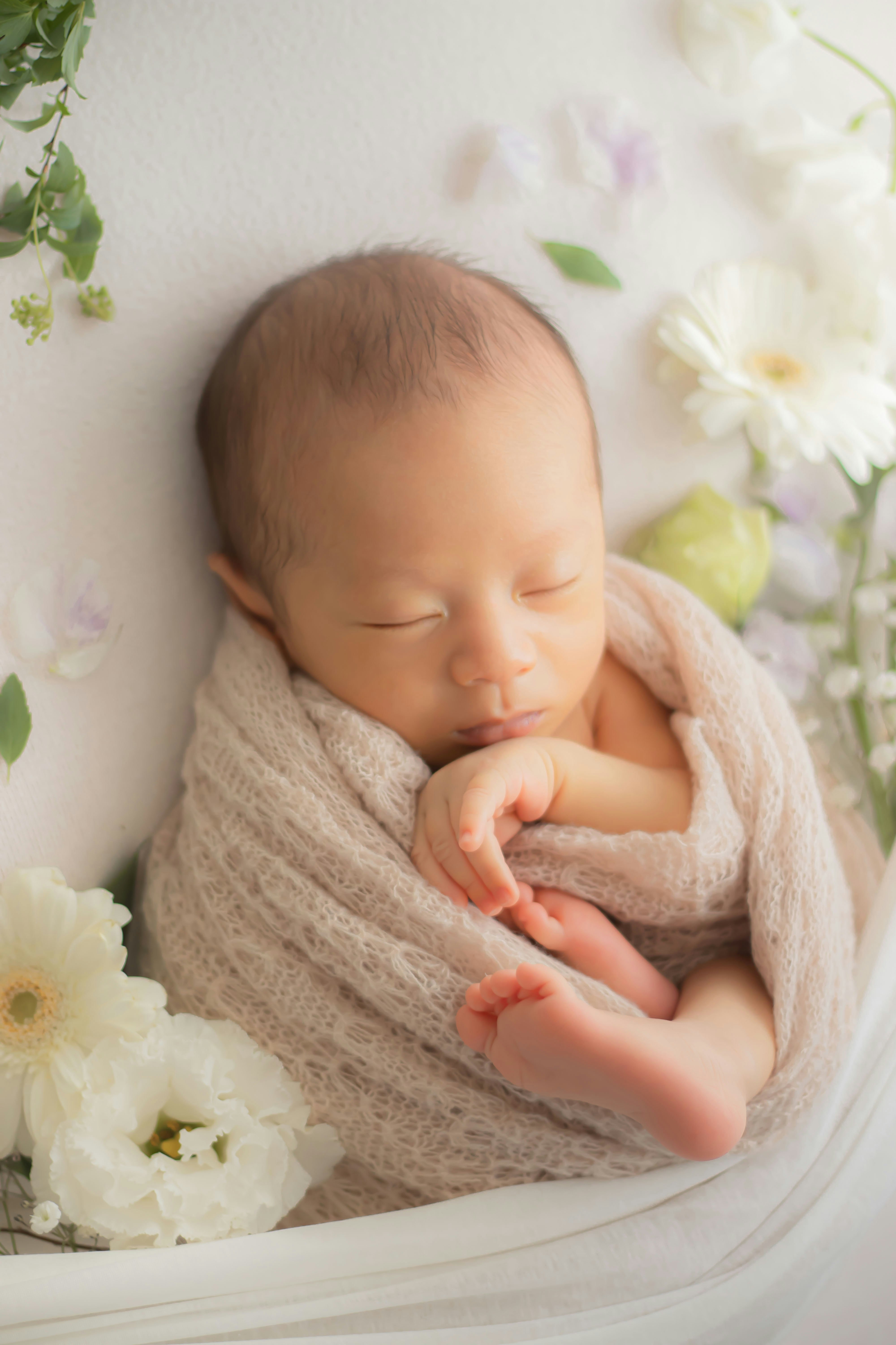生花に囲まれた新生児がふんわり包まれて眠る