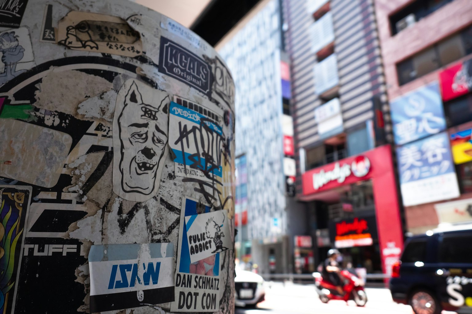 Poteau recouvert d'autocollants dans un cadre urbain avec des bâtiments et des véhicules