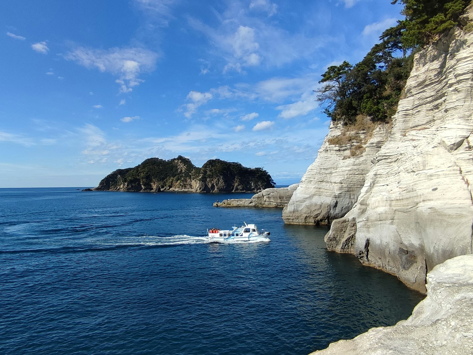 Una piccola barca che naviga in acque blu vicino a scogliere bianche e un'isola