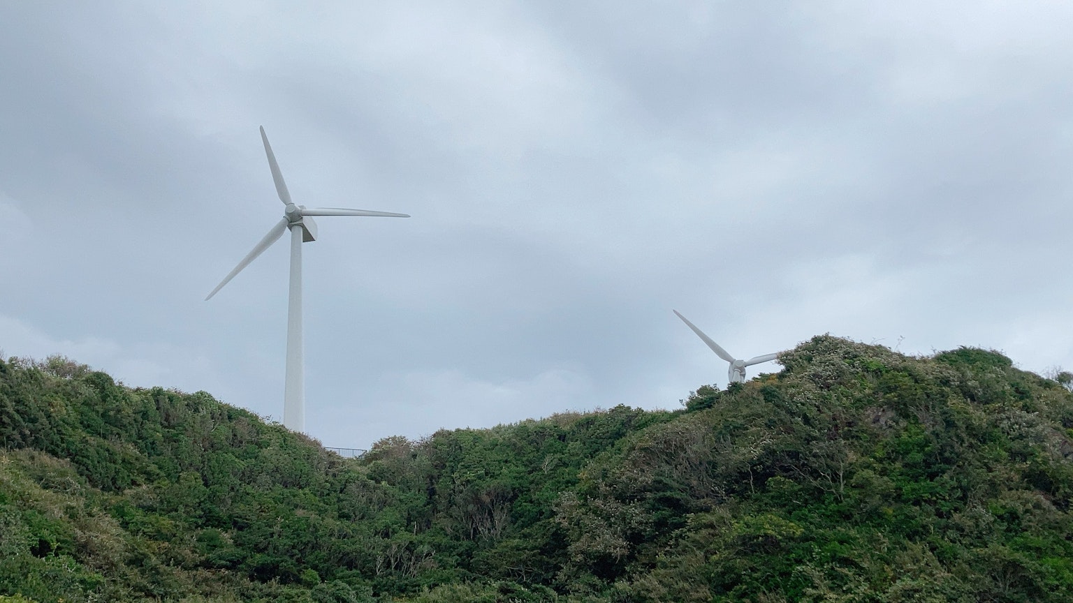 綠色丘陵上的風力發電機和陰雲