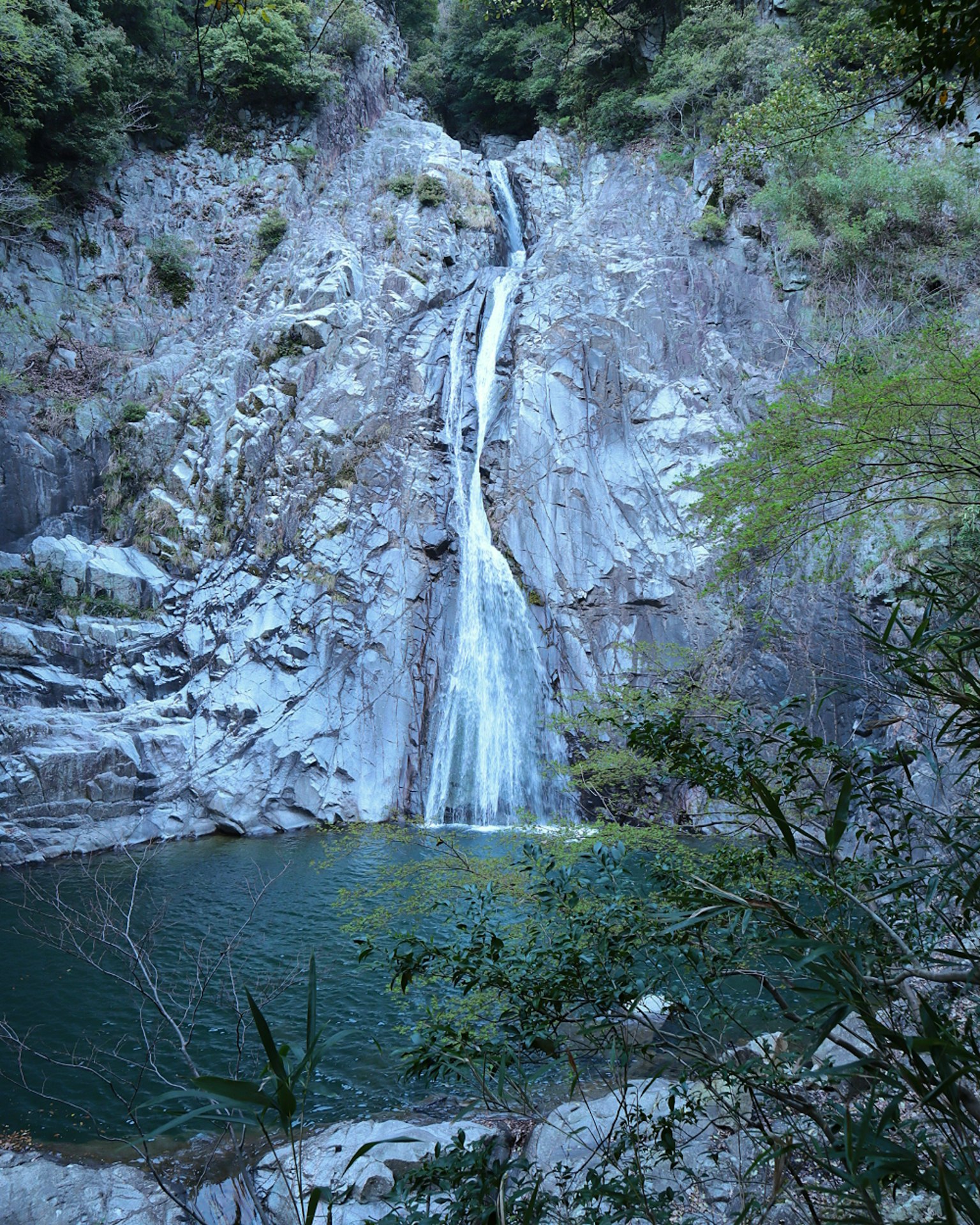 A stunning view of a waterfall cascading down rocky cliffs with tranquil blue water below