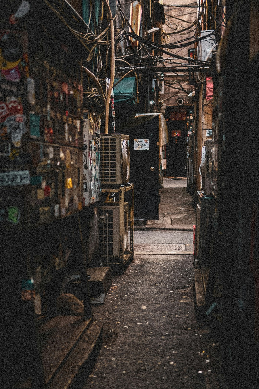 狭い路地に沿った壁に貼られたステッカーと配管が見える