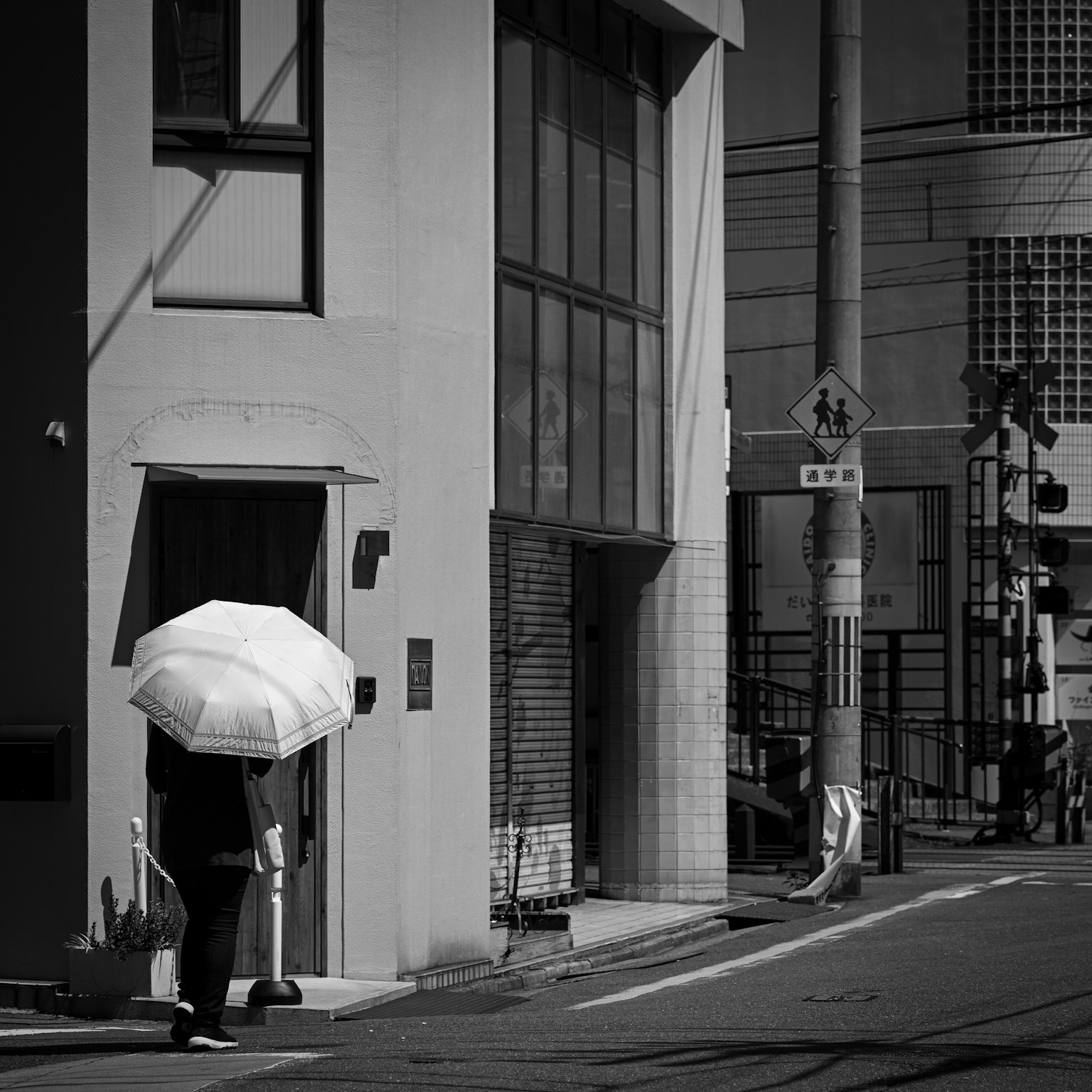 白い傘を持った人物が建物の前に立っているモノクロの街角の風景