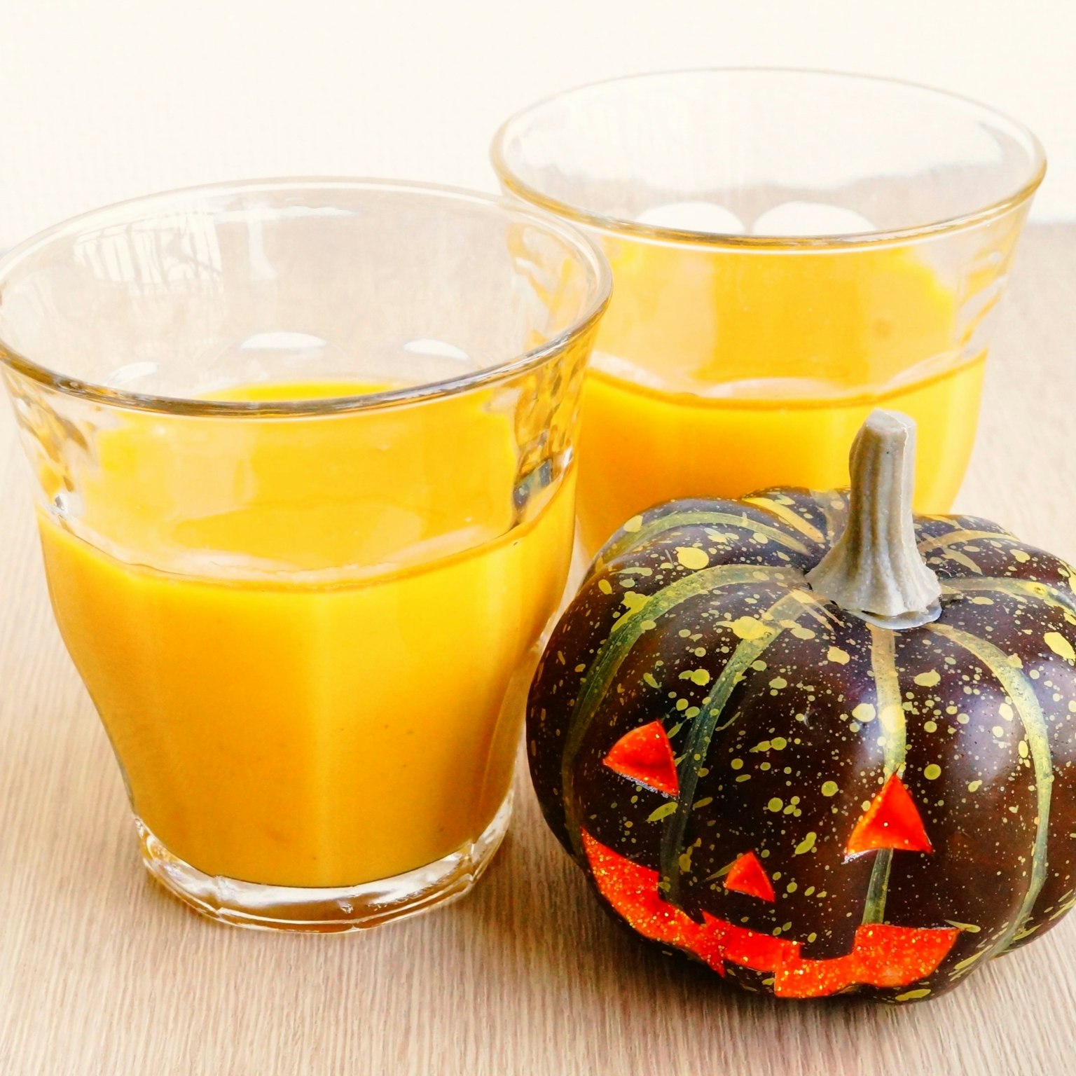Dos vasos de jugo de naranja y una calabaza de Halloween sobre una superficie de madera