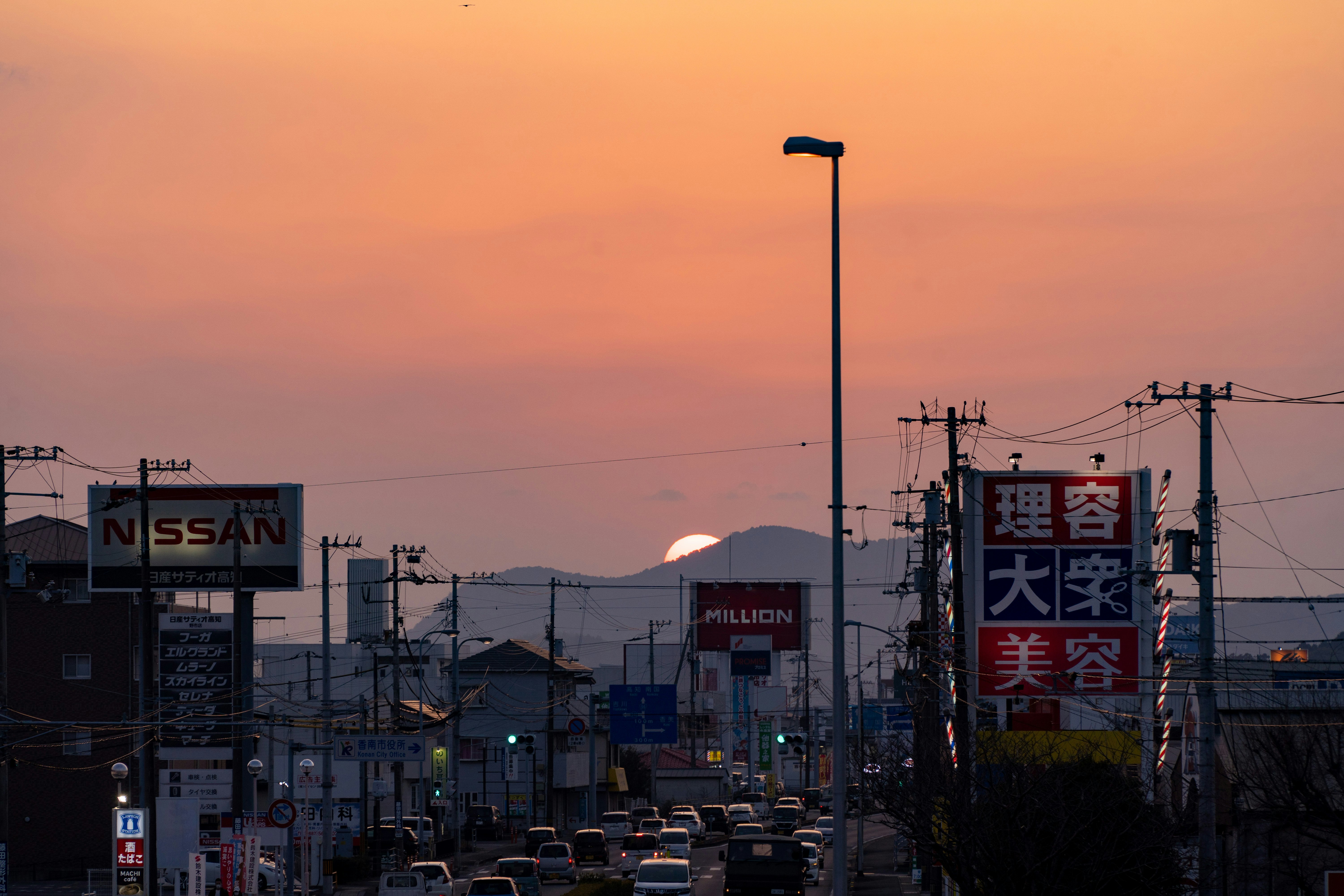 夕焼けの空と工業地帯の看板が並ぶ街並み