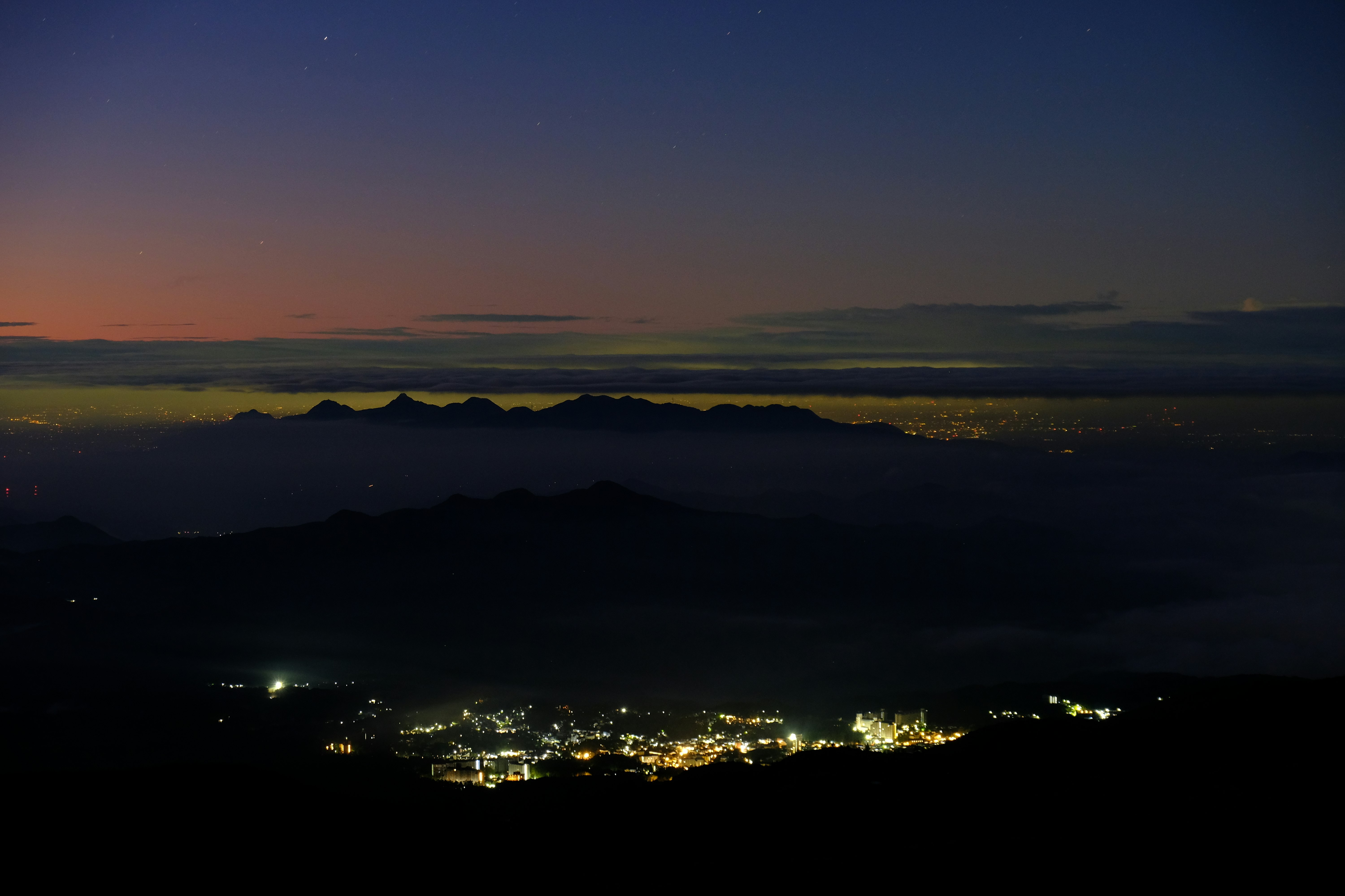夕暮れの山並みと街の夜景が広がる風景