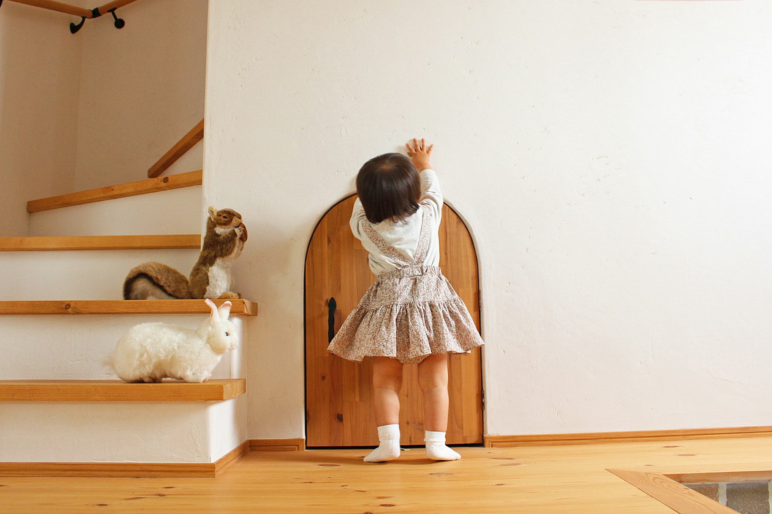 A small girl reaching for a tiny door in a cozy interior