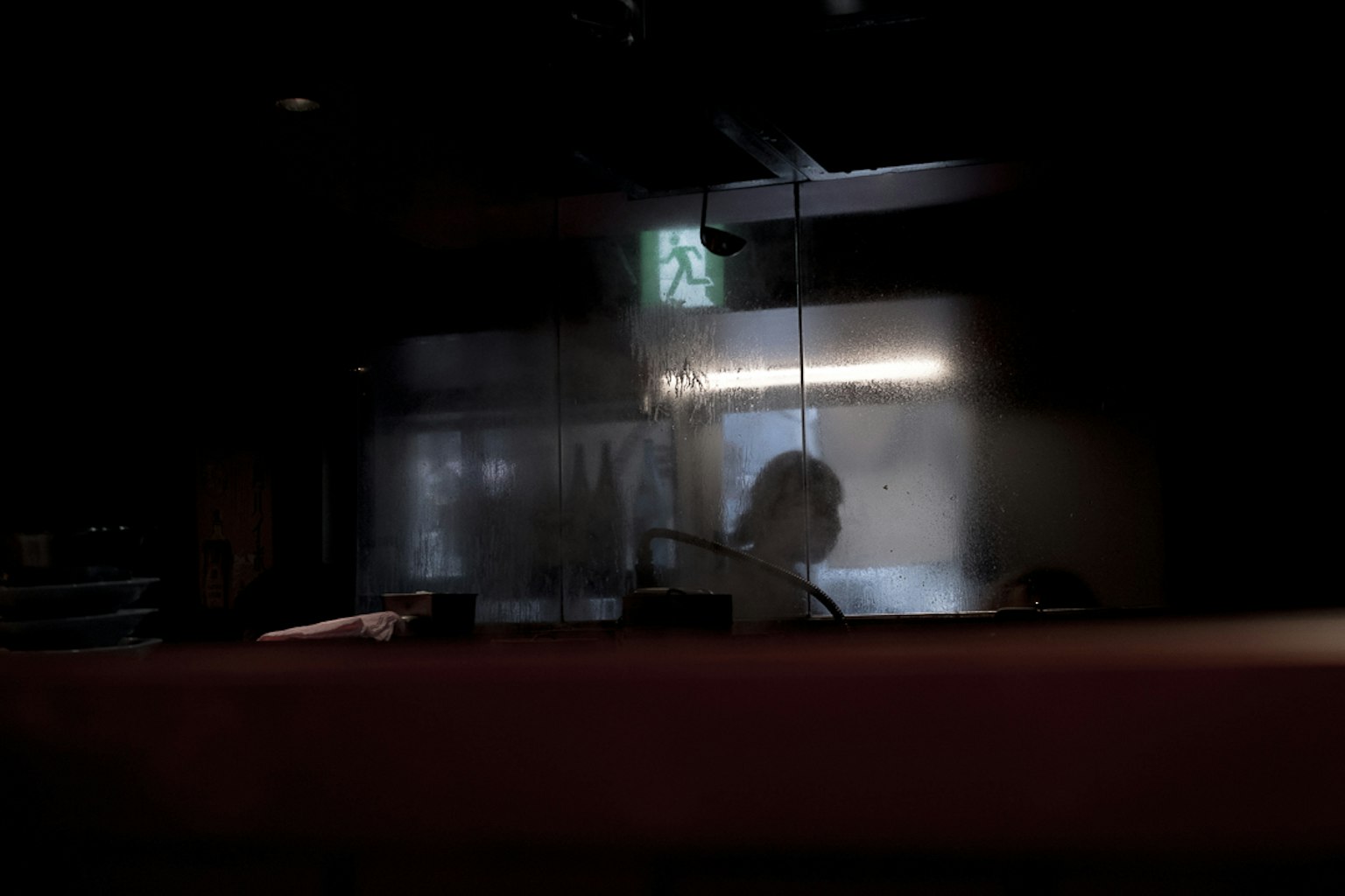 Silhouette d'une personne derrière une barrière translucide dans un espace faiblement éclairé