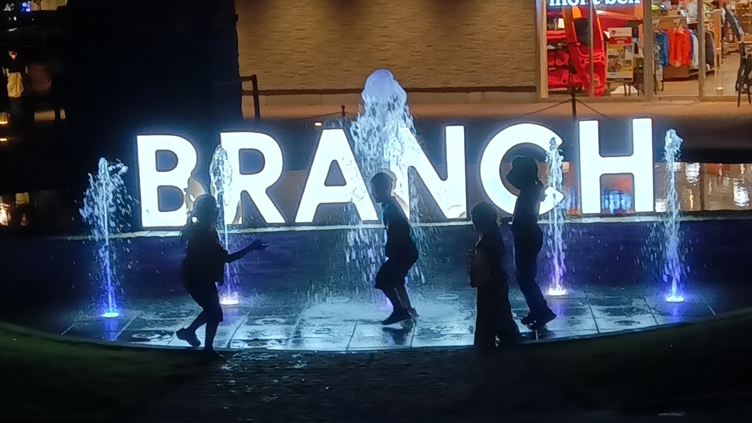夜の噴水の前で遊ぶ子供たちと大きな「BRANCH」の文字