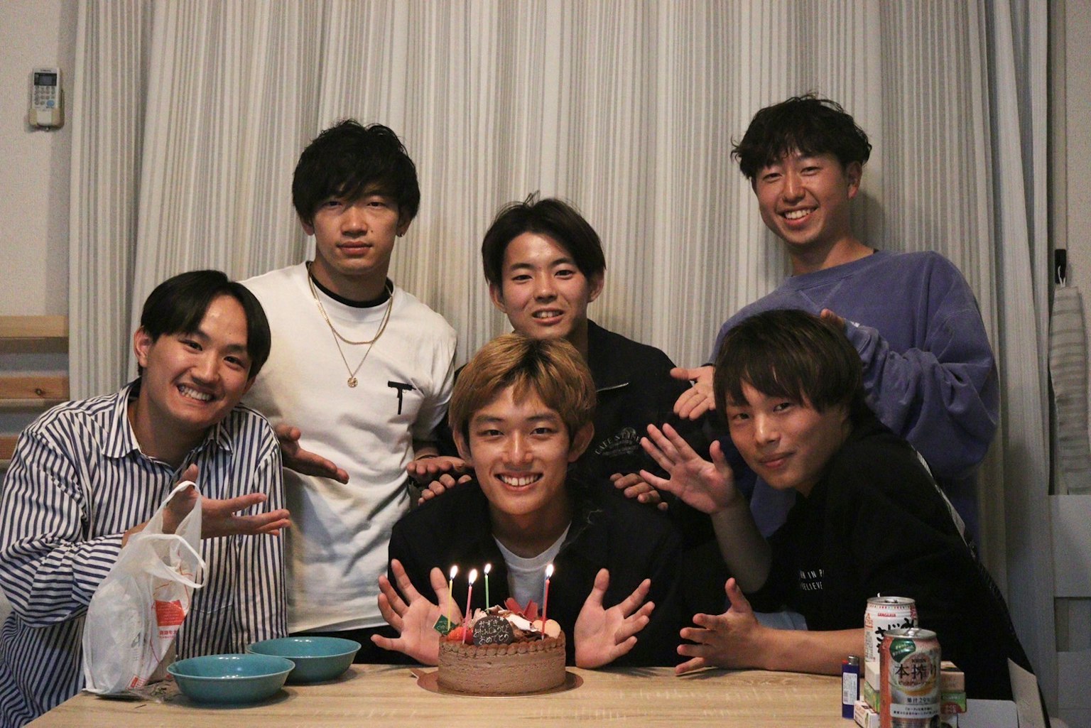 Six men gathered around a table smiling and posing