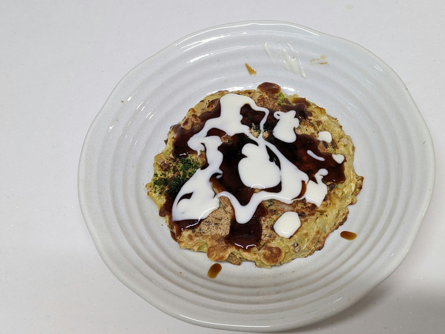 Okonomiyaki sur une assiette blanche arrosée de sauce et de mayonnaise