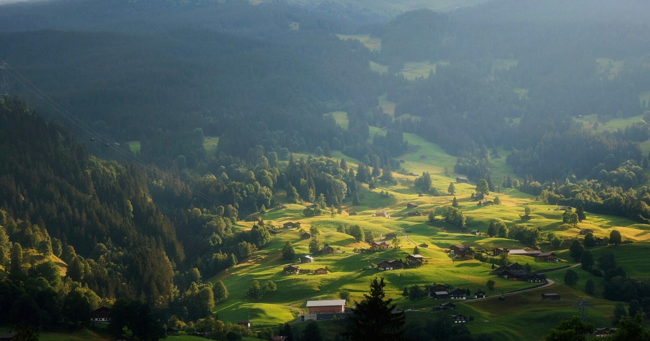 Luftaufnahme eines grünen Tals mit Weiden und kleiner Siedlung