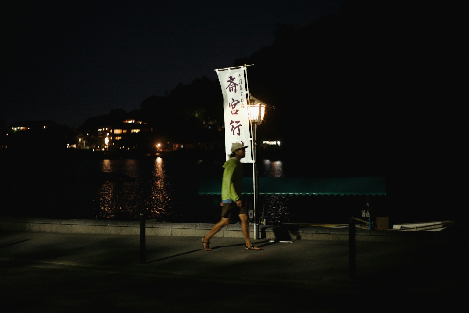 Personne marchant avec un drapeau le long de la rivière la nuit avec des lumières en arrière-plan