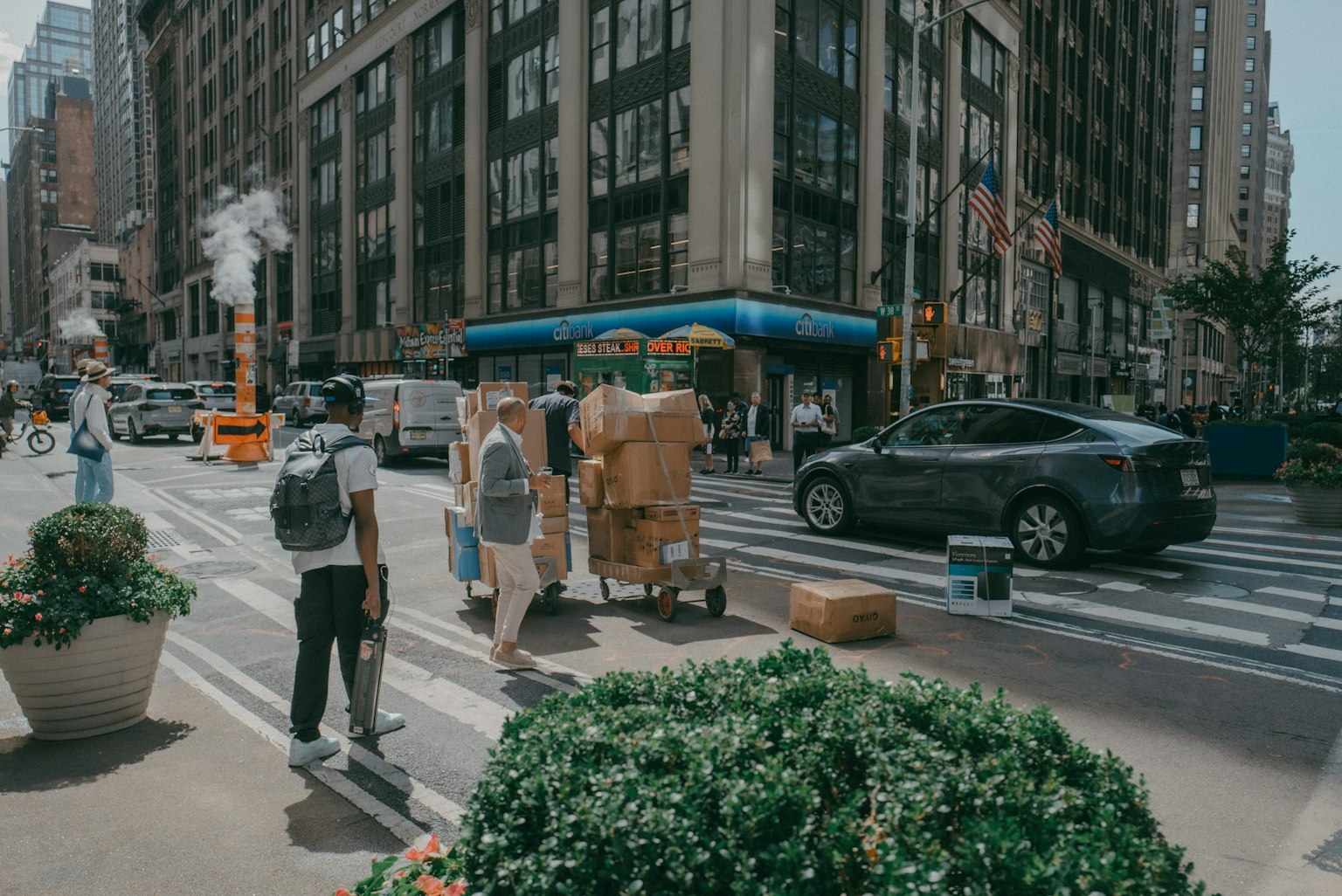 People transporting goods on a city street with vehicles and buildings in the background