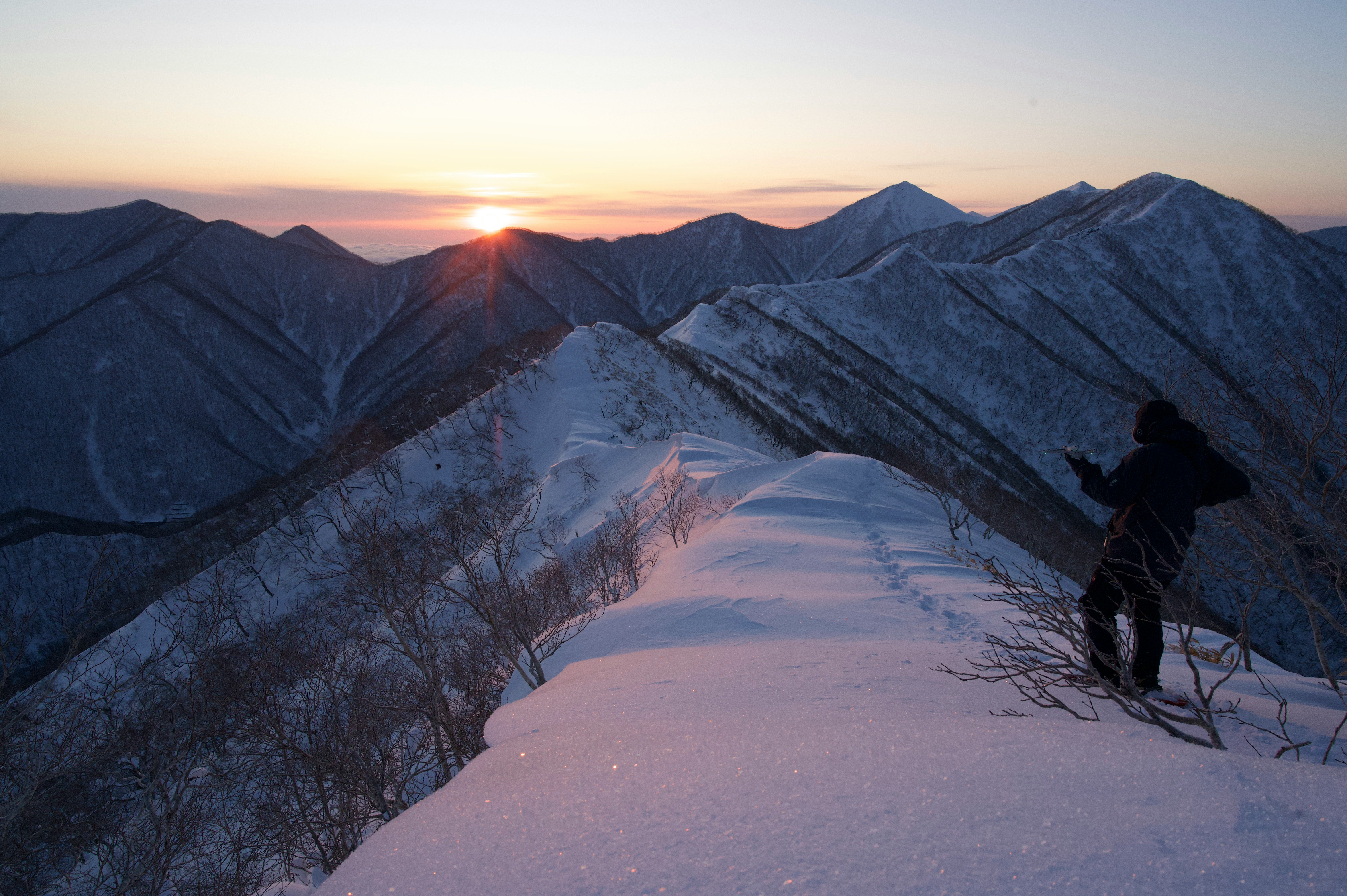 夕焼けの稜線と雪山のトレイル、歩く人影