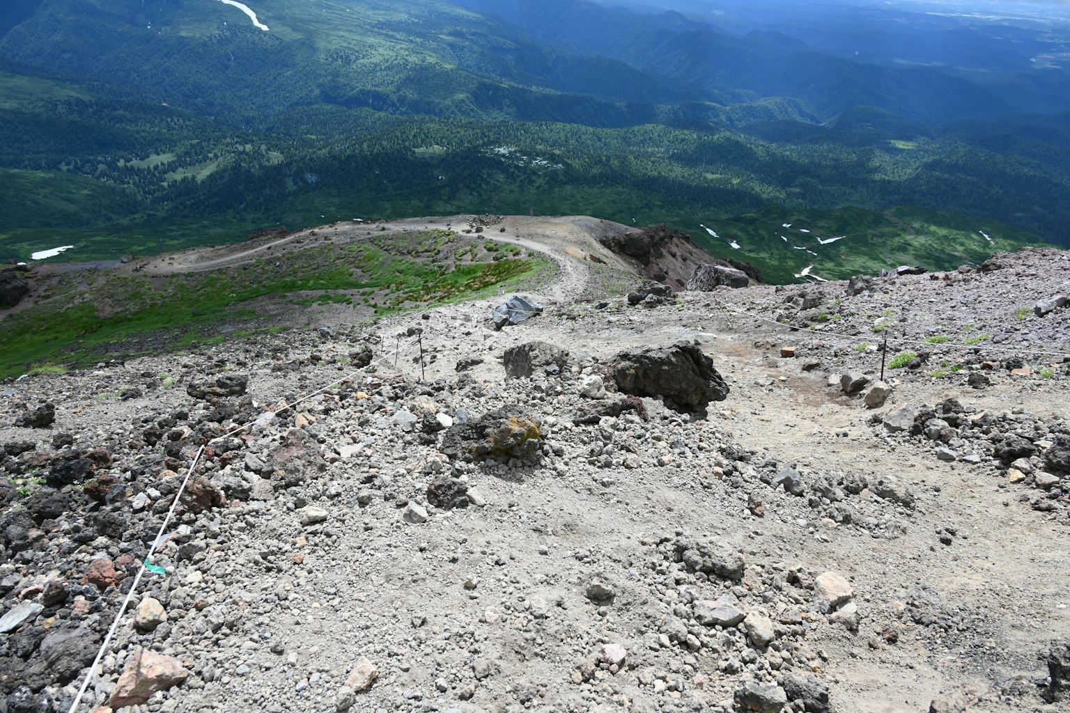 View from the mountain peak showing a rocky path and lush greenery below