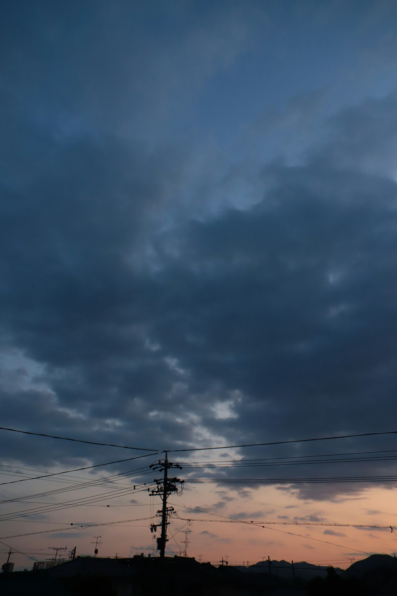 Silhouette of a utility pole against a sunset sky with dramatic clouds