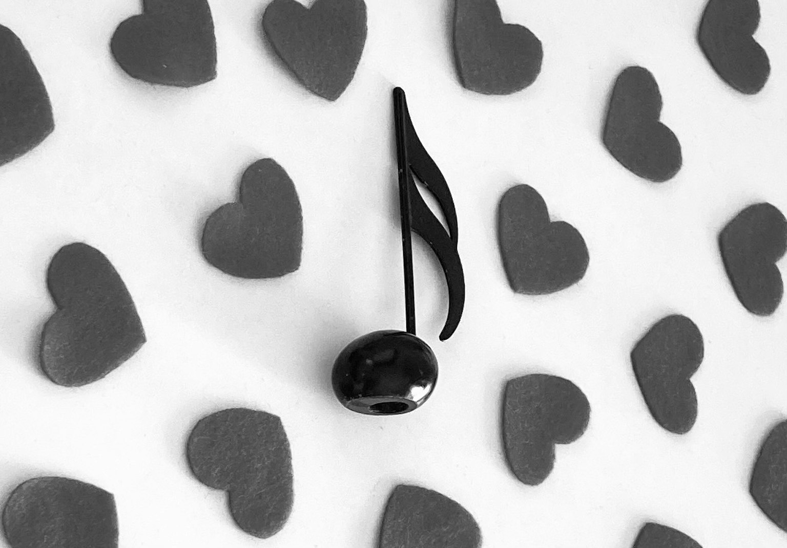 Una nota musical negra sobre un fondo de formas de corazón en escala de grises