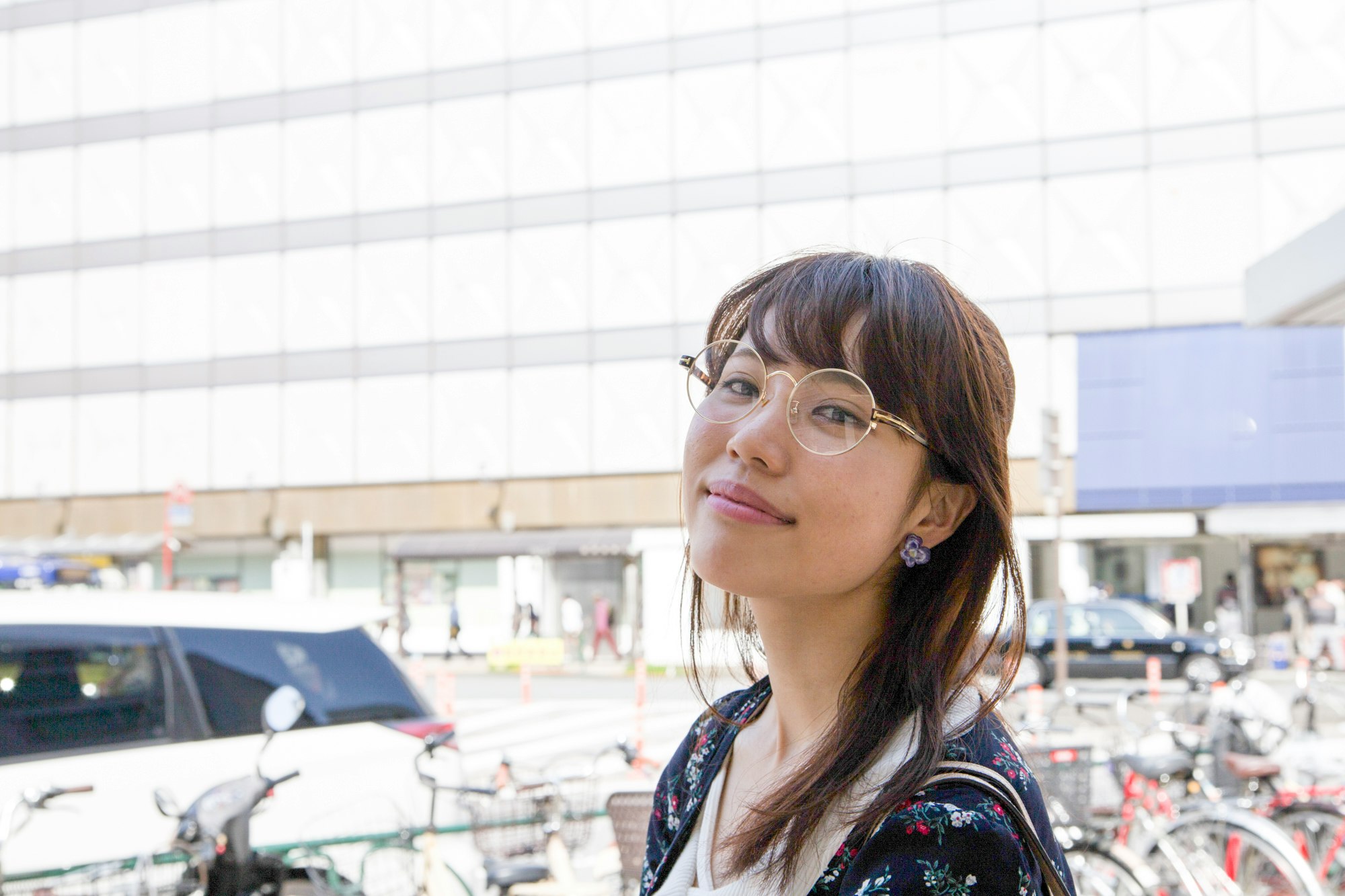 屋外の自転車が並ぶ駅前で微笑む女性
