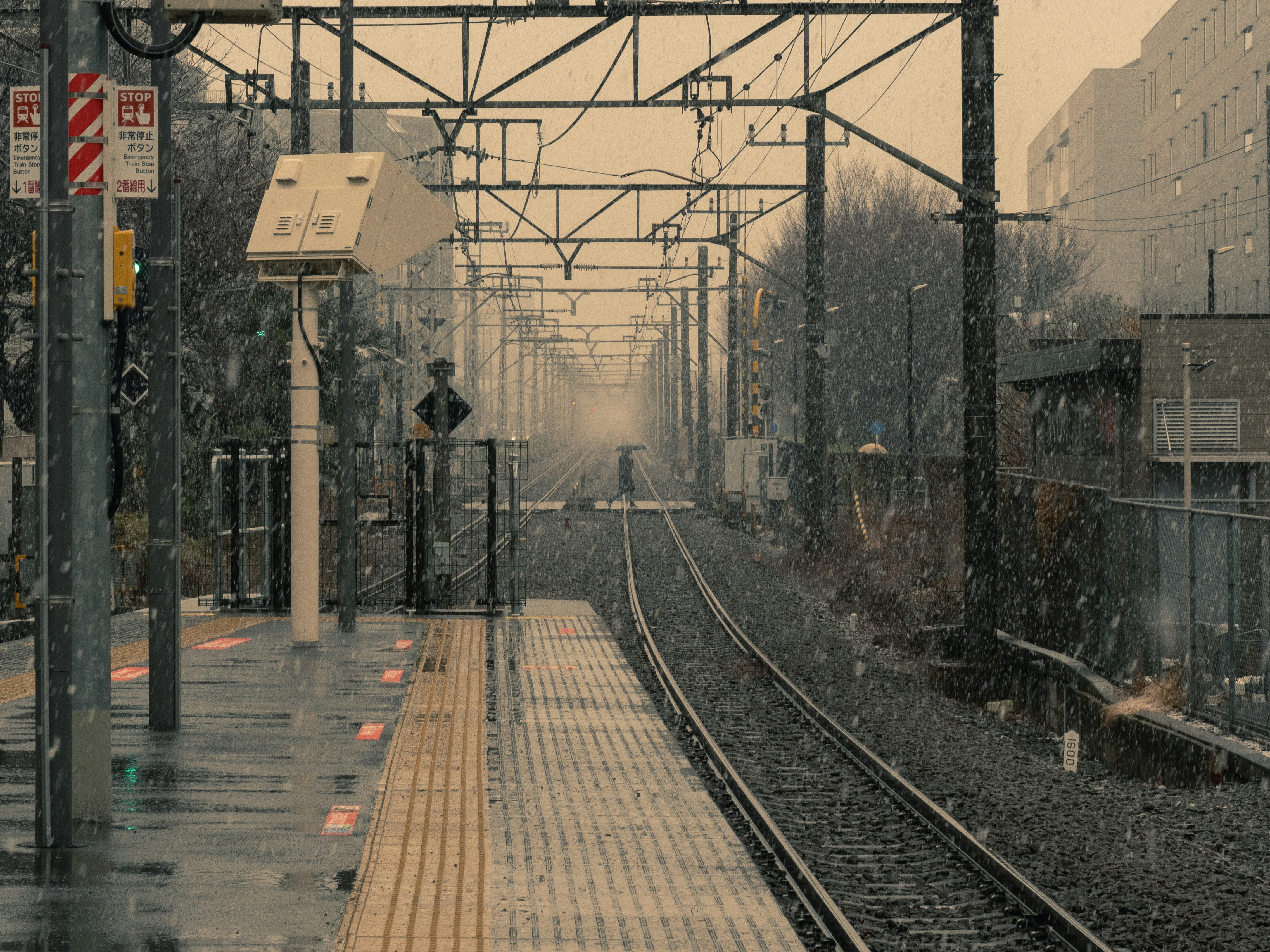 雪の降る踏切と線路のある駅前の街並み