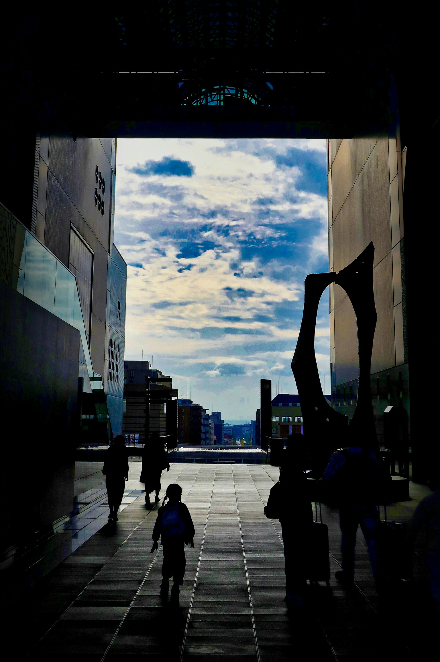 青空と雲が見えるアーチ型の通路を歩く人々と子供のシルエット
