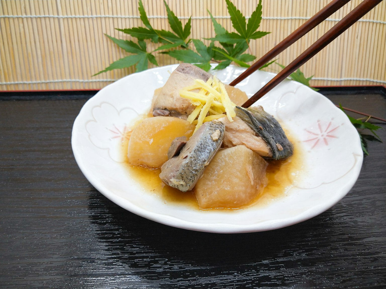 一個白色的盤子，盛著日本炖魚和蘿蔔，上面裝飾著生薑