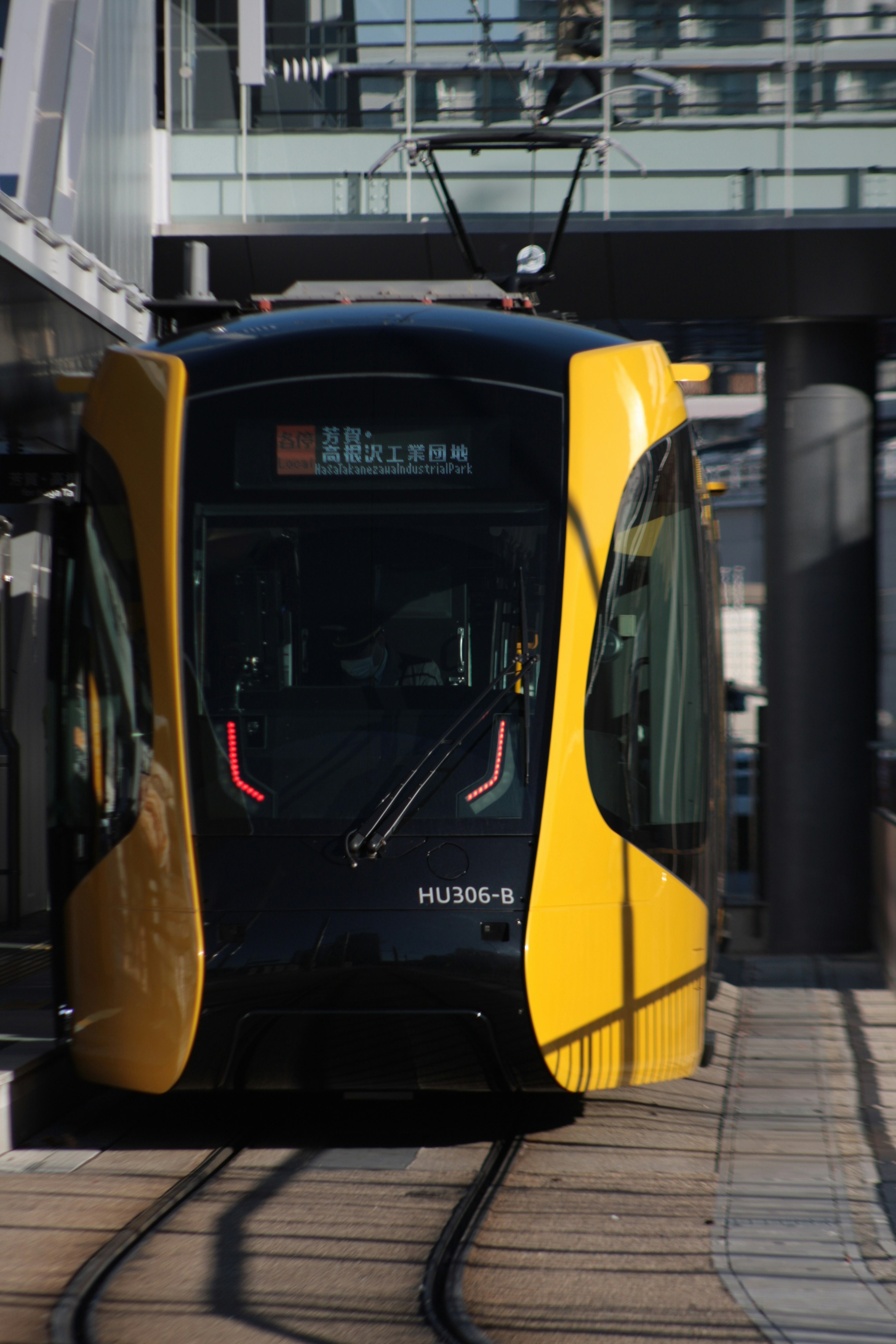 高架駅のホームに停車する黄色い電車の前面