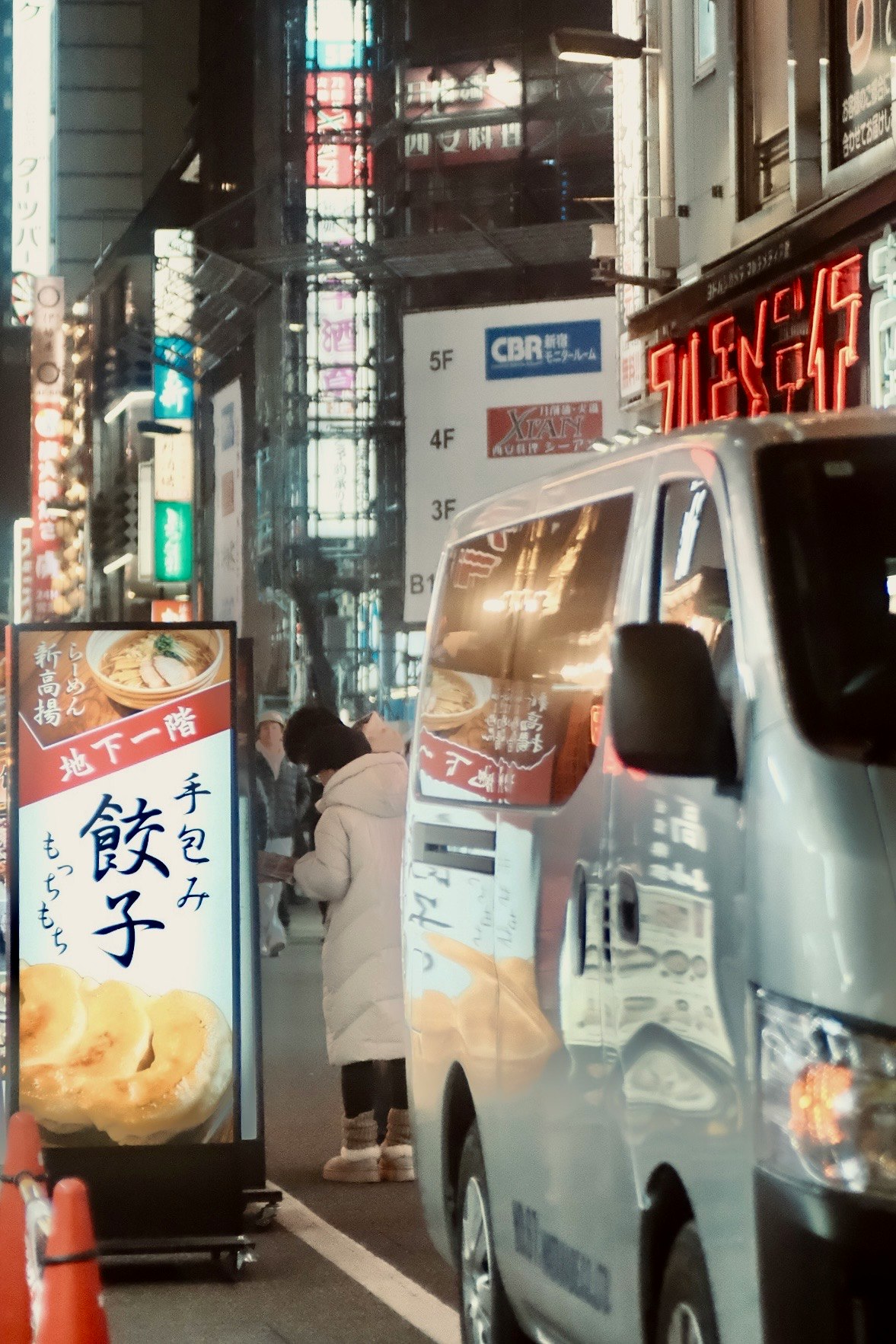 路地の屋台前に停まる白い軽トラックと看板のある街並み