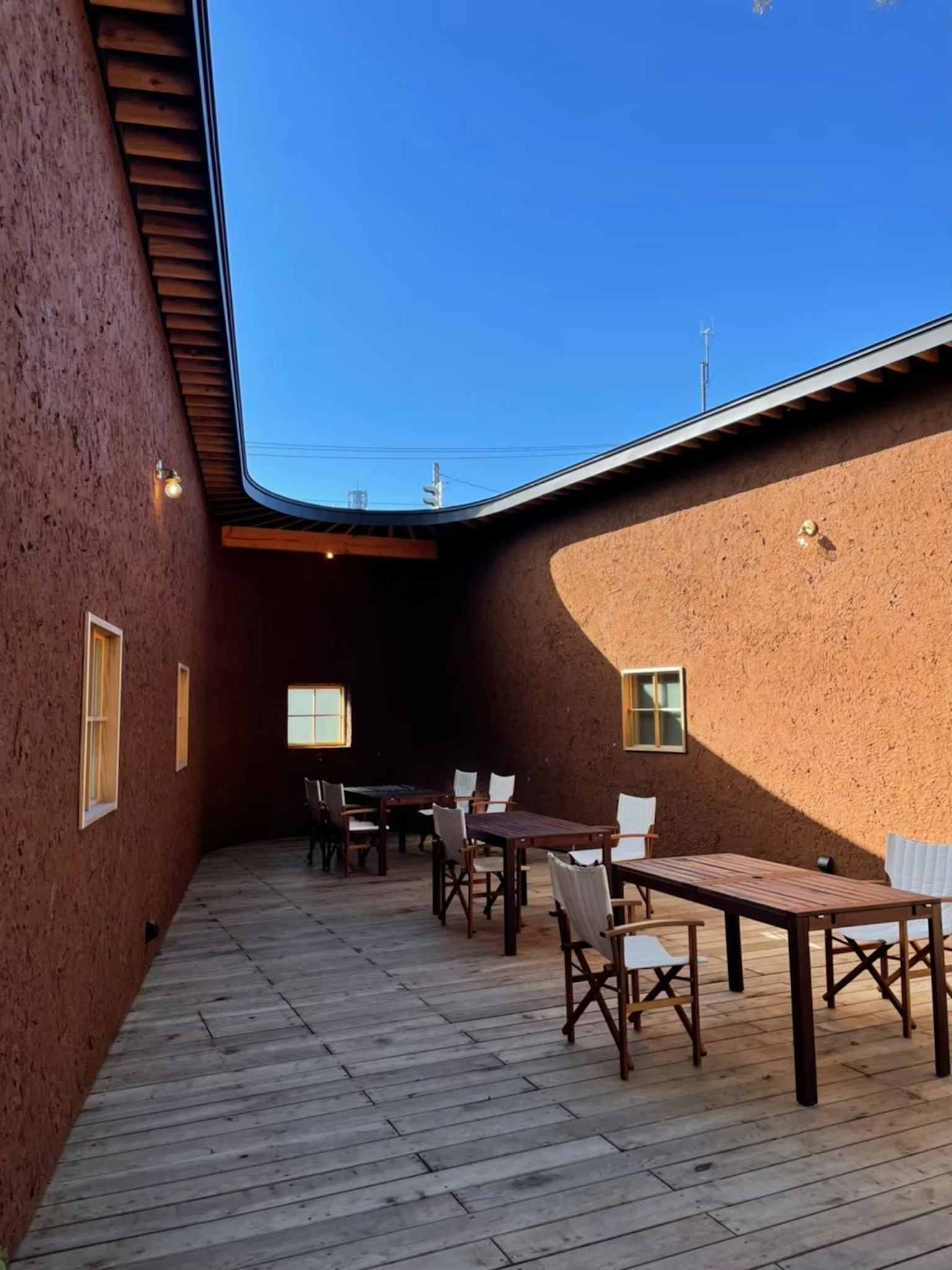 Espace extérieur avec des murs brun rougeâtre et des tables en bois